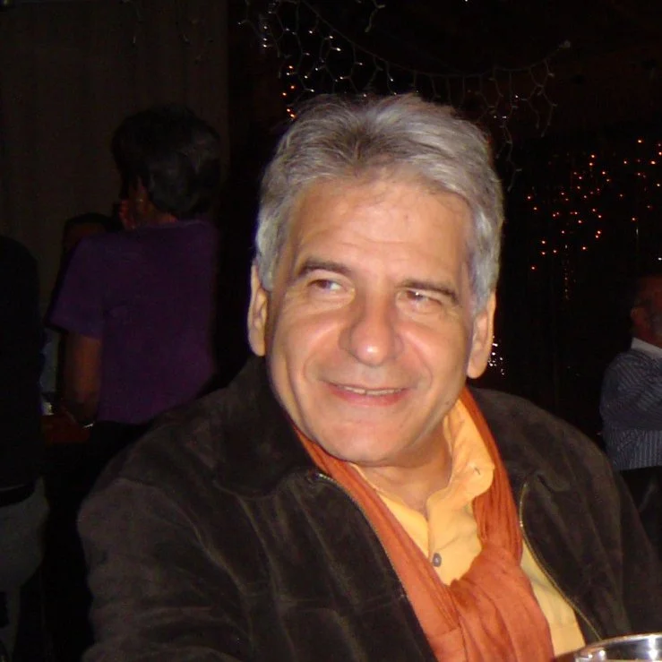 A middle-aged man with gray hair smiling at a party or social gathering; dark background with string lights.