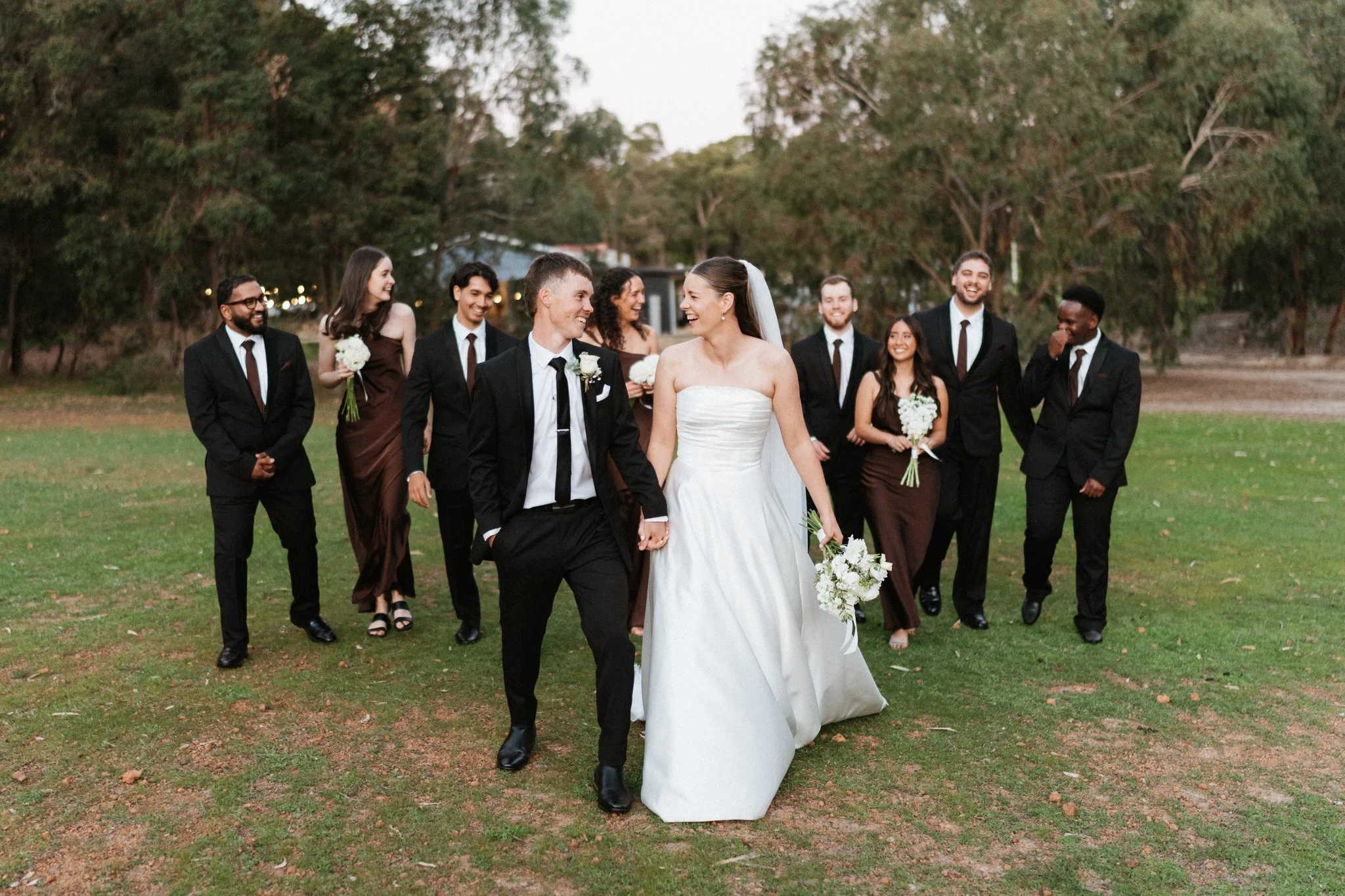 Bride and groom walking across a lawn with their bridal party behind them