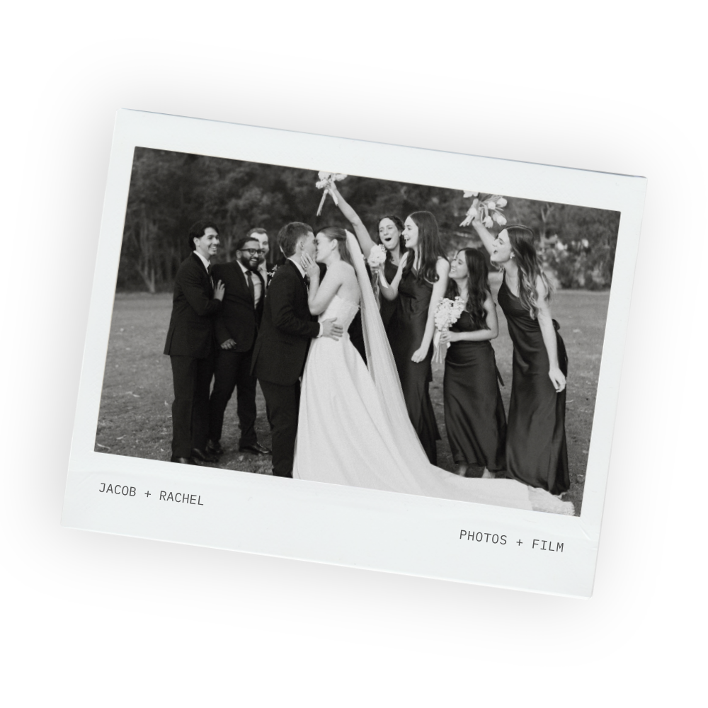 Black and white photo of bride and groom kissing as their bridal party cheers