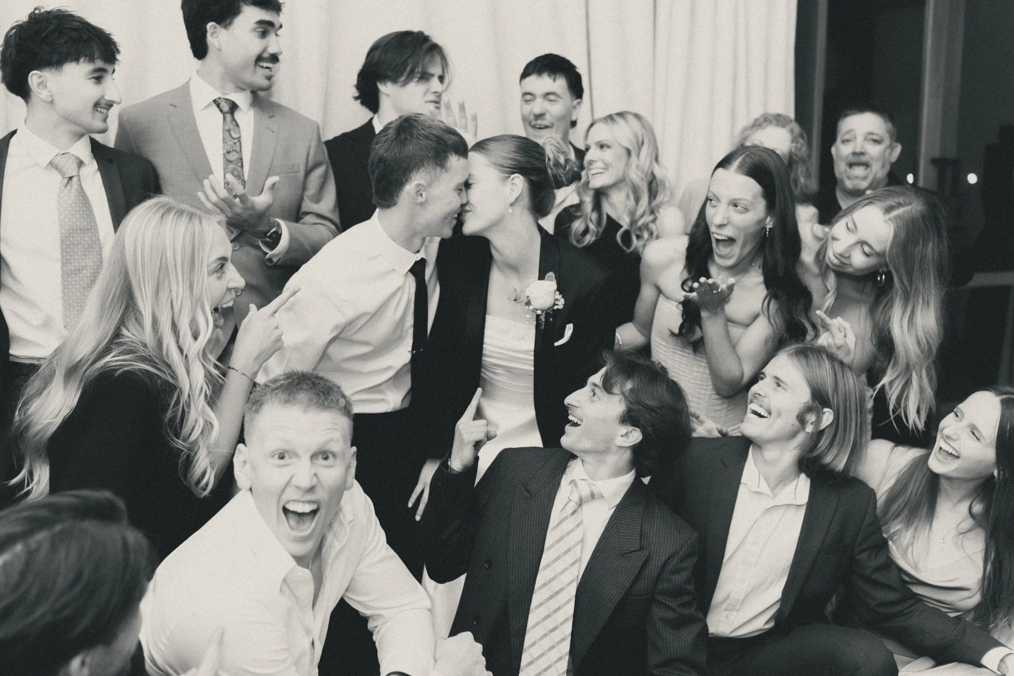 Black and white photo of guests cheering as the couple kiss at the reception