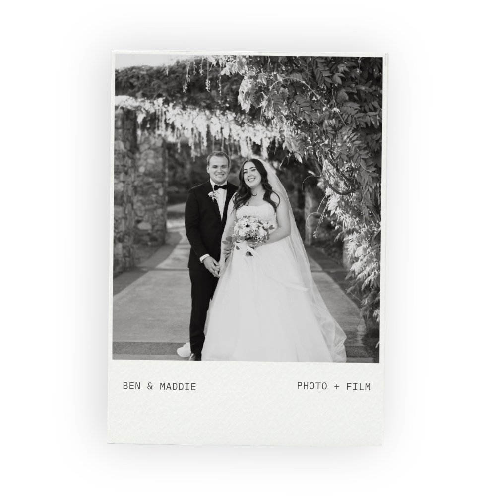 Black and white photo of bride and groom under a flowering arbour