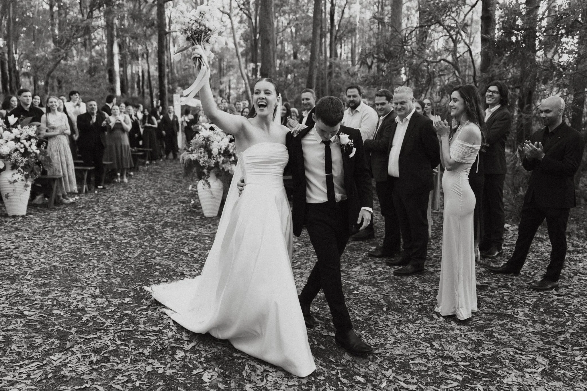Black and white photo of newlyweds cheering as they walk back down the aisle