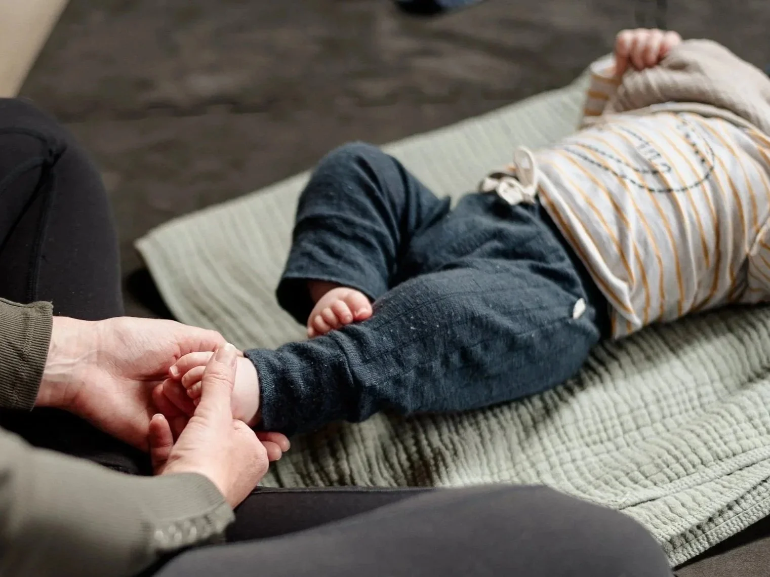 A young baby lying on a blanket, an adult massaging its foot.