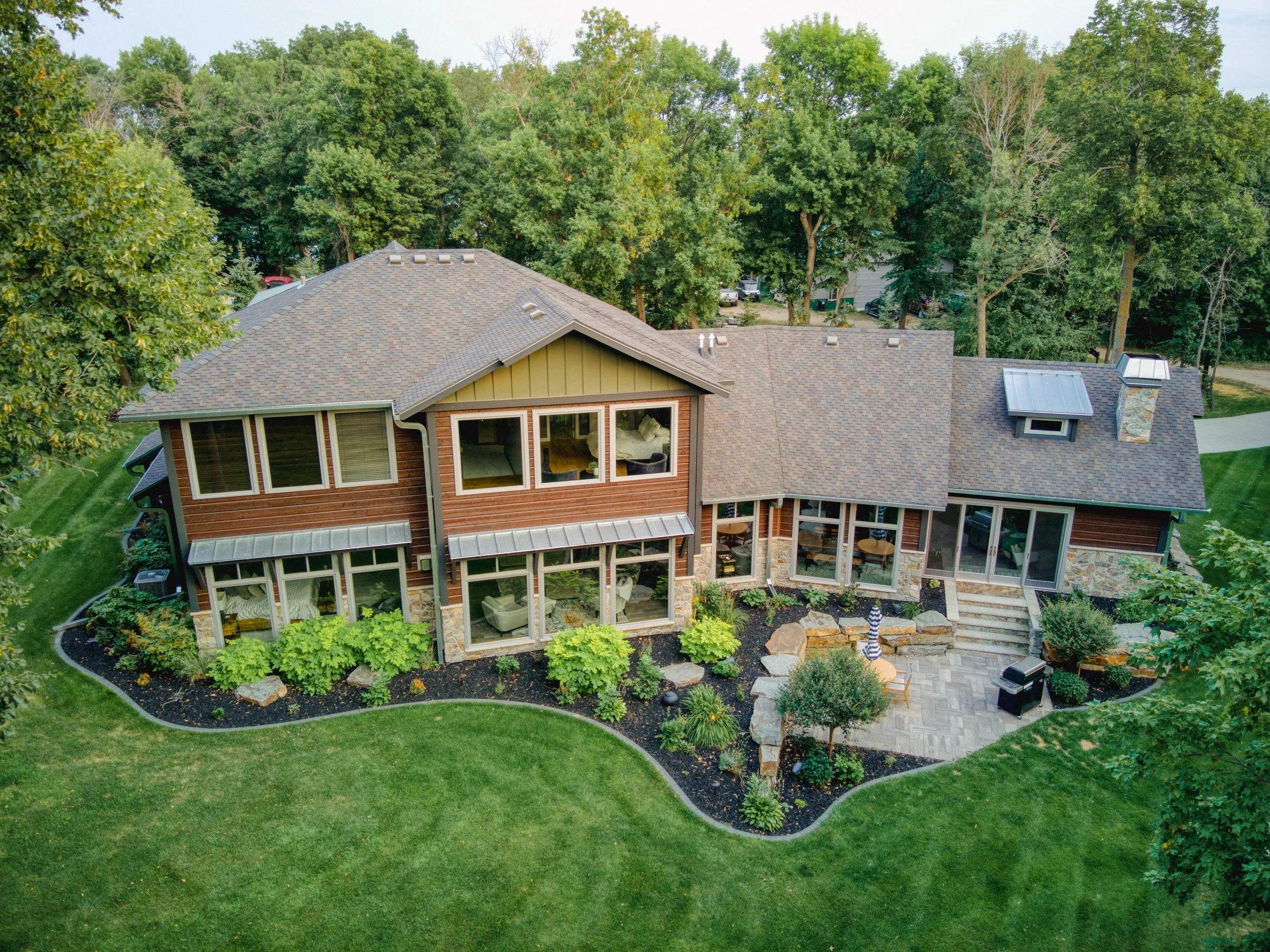 An aerial view of a modern house with large windows, surrounded by a landscaped garden and greenery, including trees and lawn.