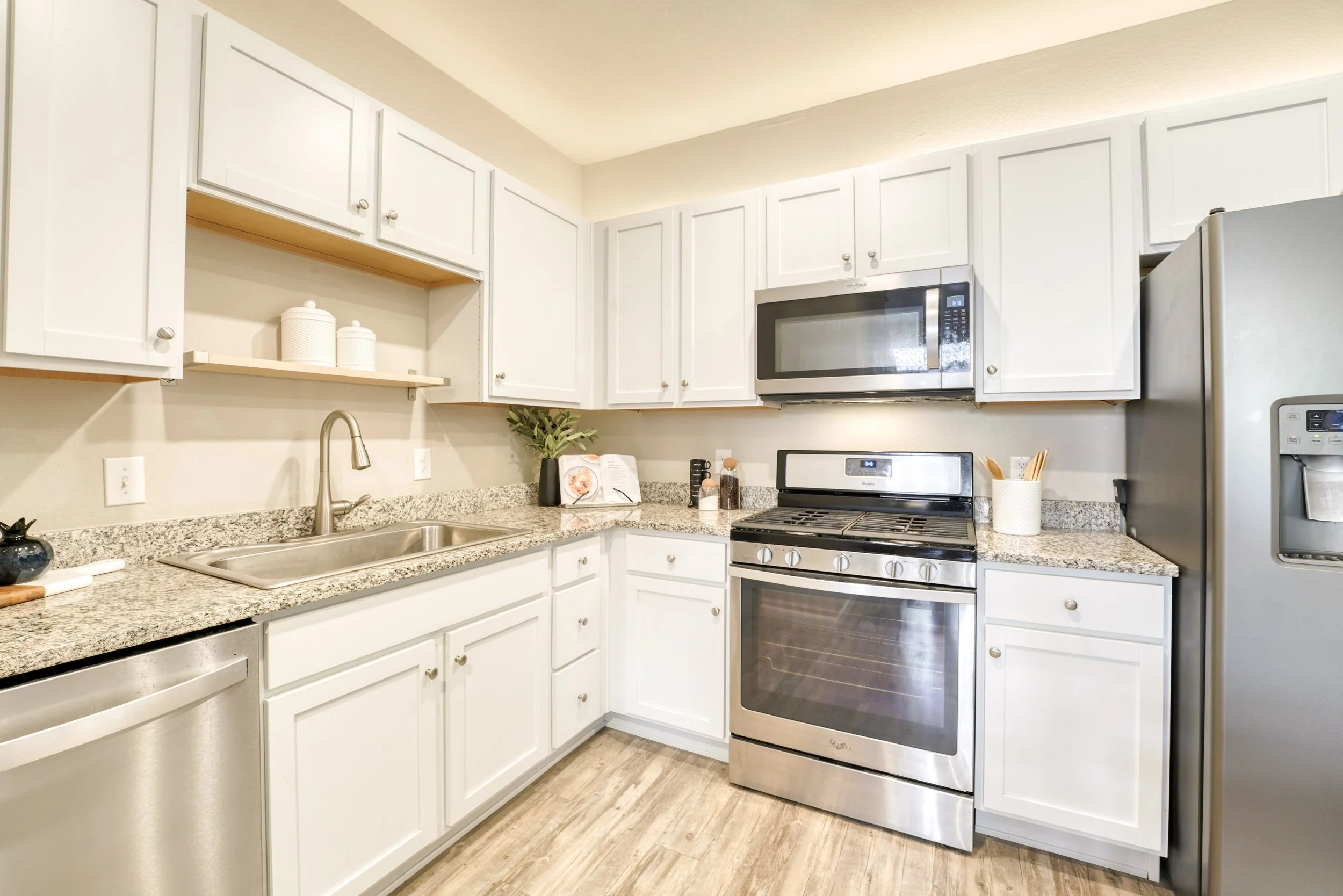 Kitchen with white cabinets, granite countertops, stainless steel appliances including a microwave, stove, and refrigerator, decorated with a plant and kitchen accessories.