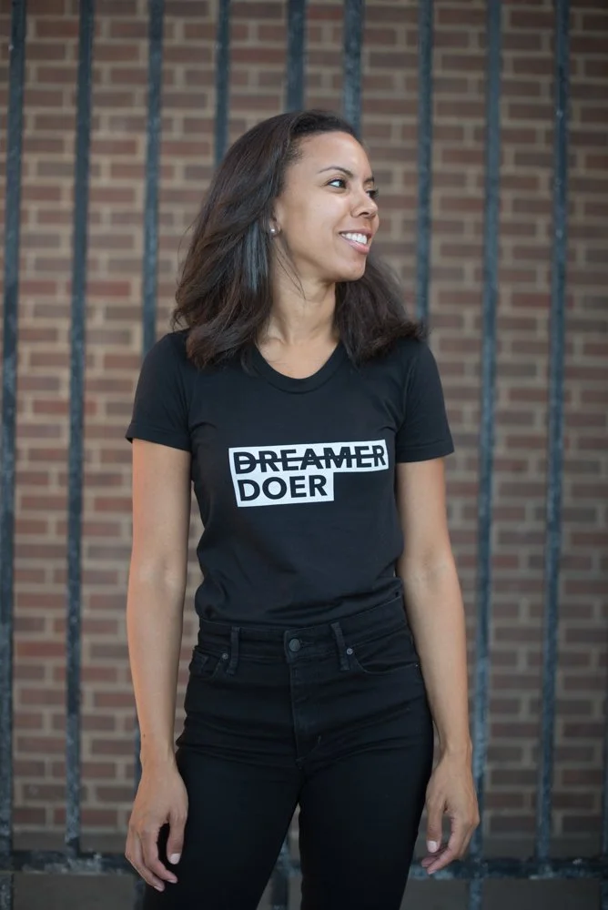 Woman with shoulder-length brown hair wearing a black T-shirt with 