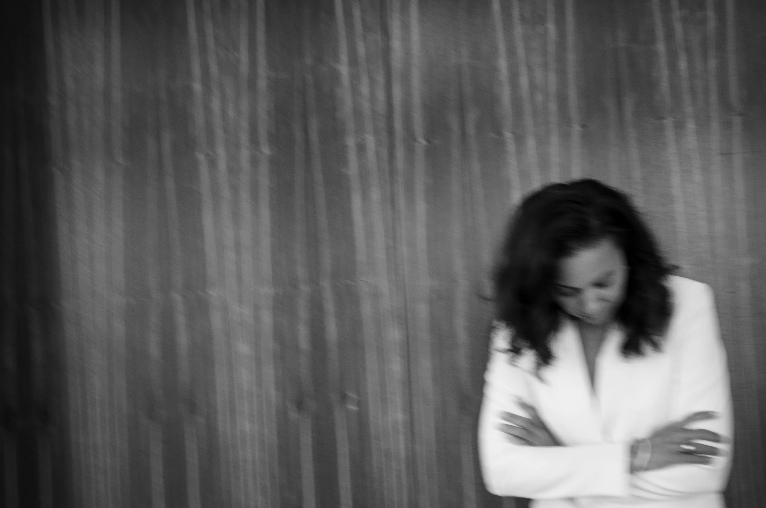 Black and white photo of a woman with long dark hair smiling, seated against a textured curtain backdrop.