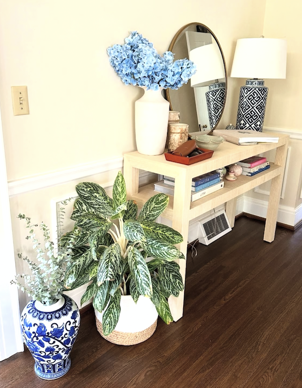 Console table styled with blue and white decor, flowers, plants, and a mirror.