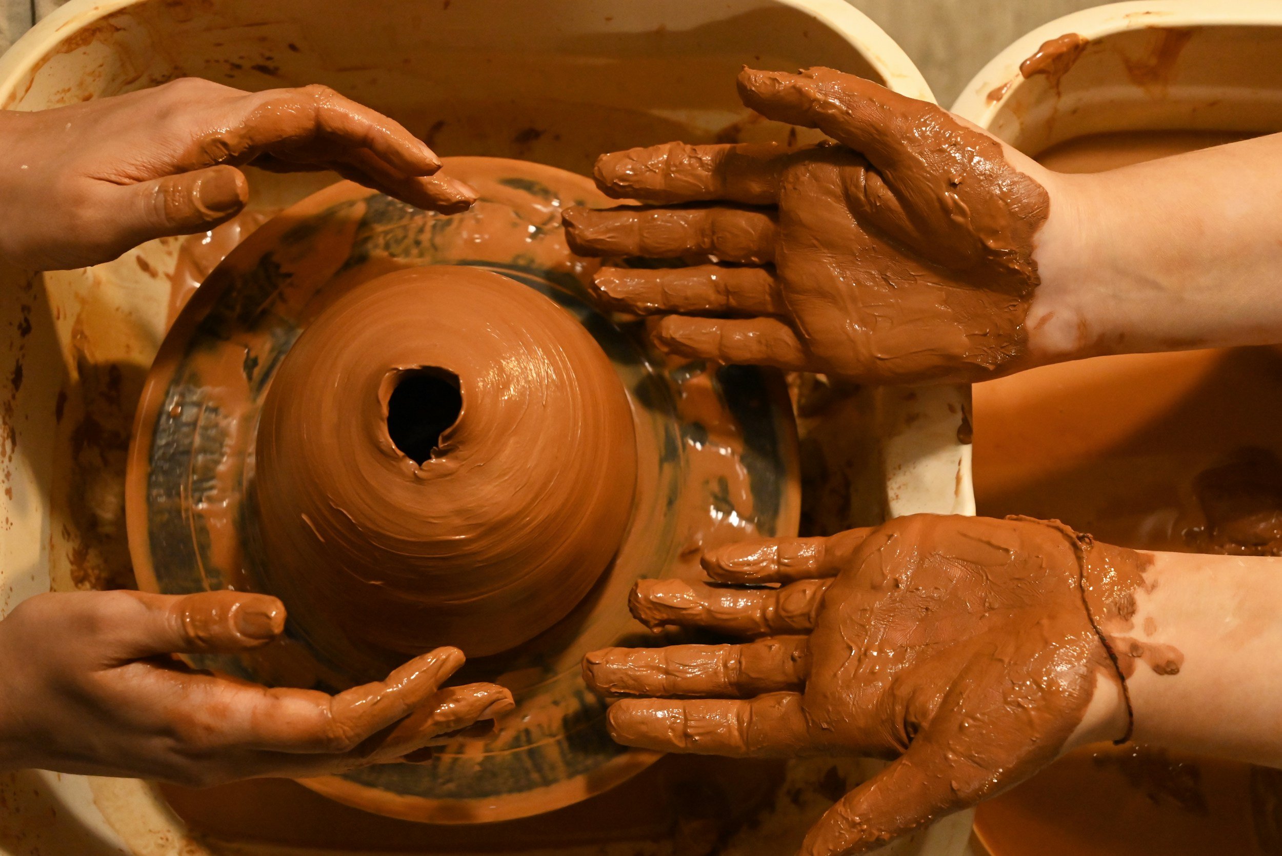 Hands shaping wet clay on a pottery wheel in a dimly lit room.