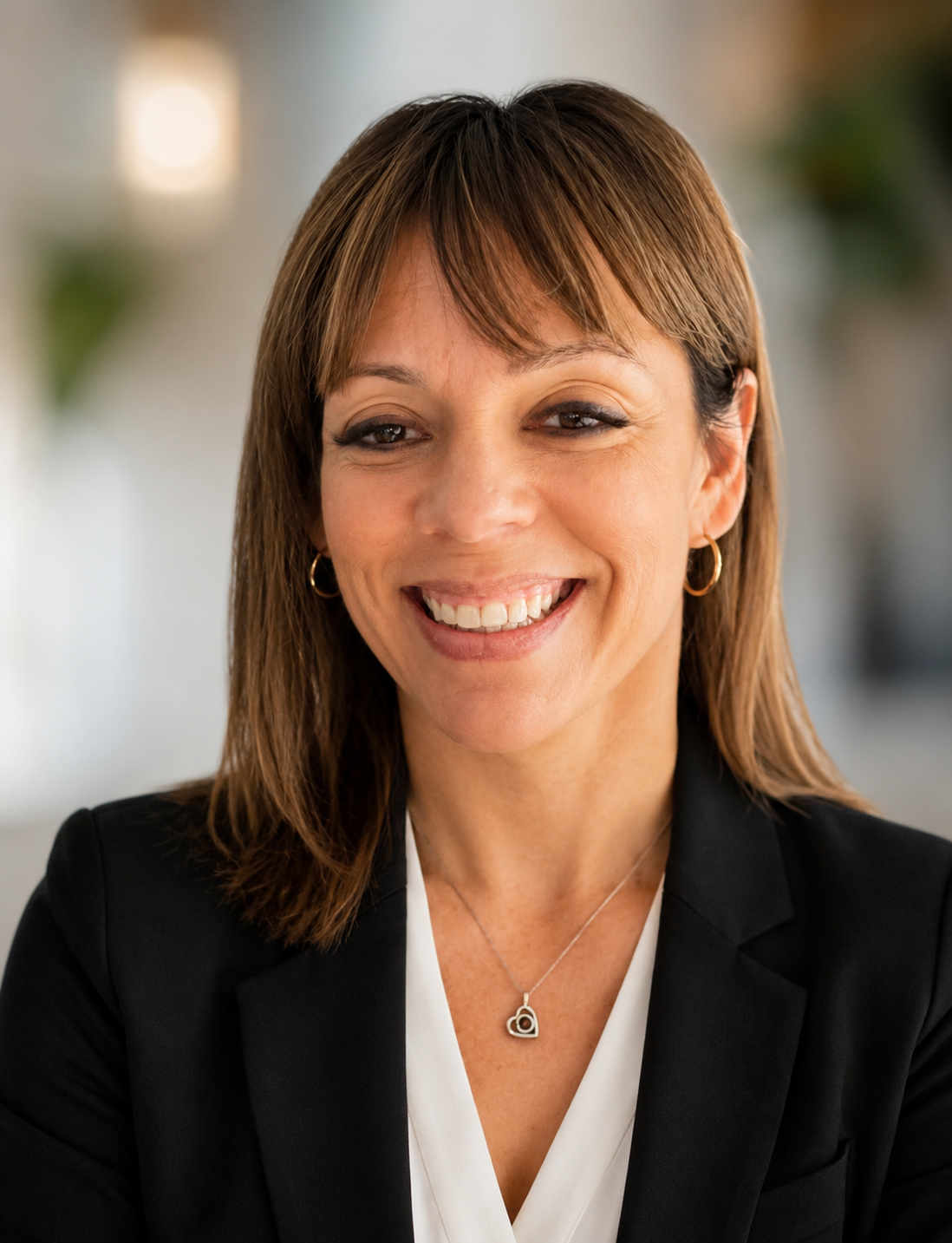 A smiling woman with brown hair, wearing earrings, a necklace, a white blouse, and a black blazer.