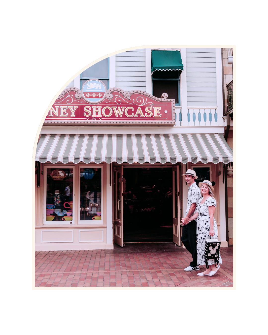 People standing in front of the opening of a shop with a sign that says 'Mickey Showcase', featuring pink and white striped awning and pastel-colored building exterior.