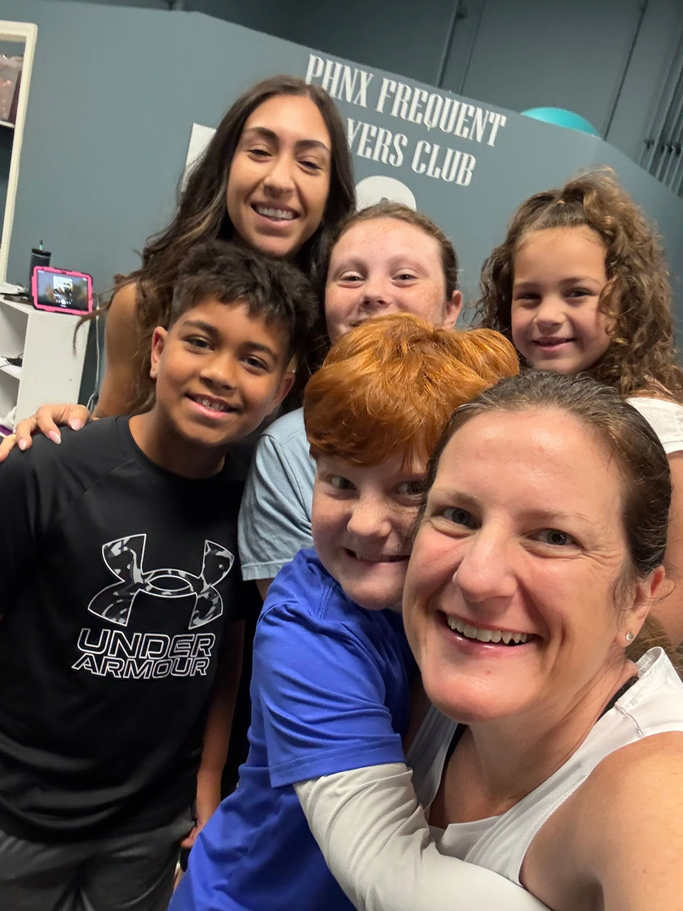 A group of people, including a woman and several children, taking a close-up selfie indoors at the Phoenix Frequent Flyers Club, smiling and showing camaraderie.