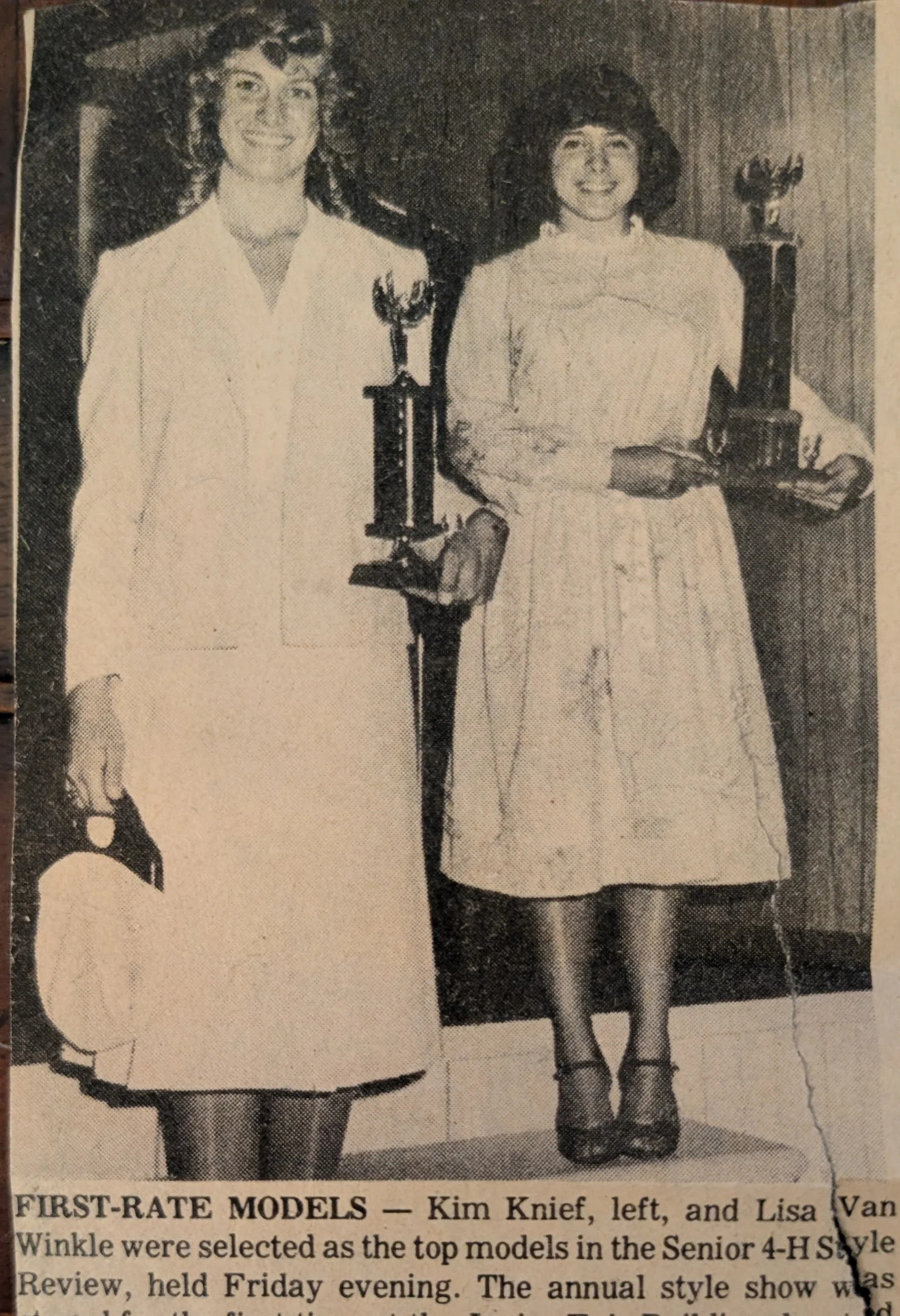 Photograph of two women, identified as Kim Knief on the left and Lisa Van Winkle, holding awards or trophies, standing indoors in front of a wooden wall with a flower arrangement on a table behind them. The image appears to be a newspaper clipping.