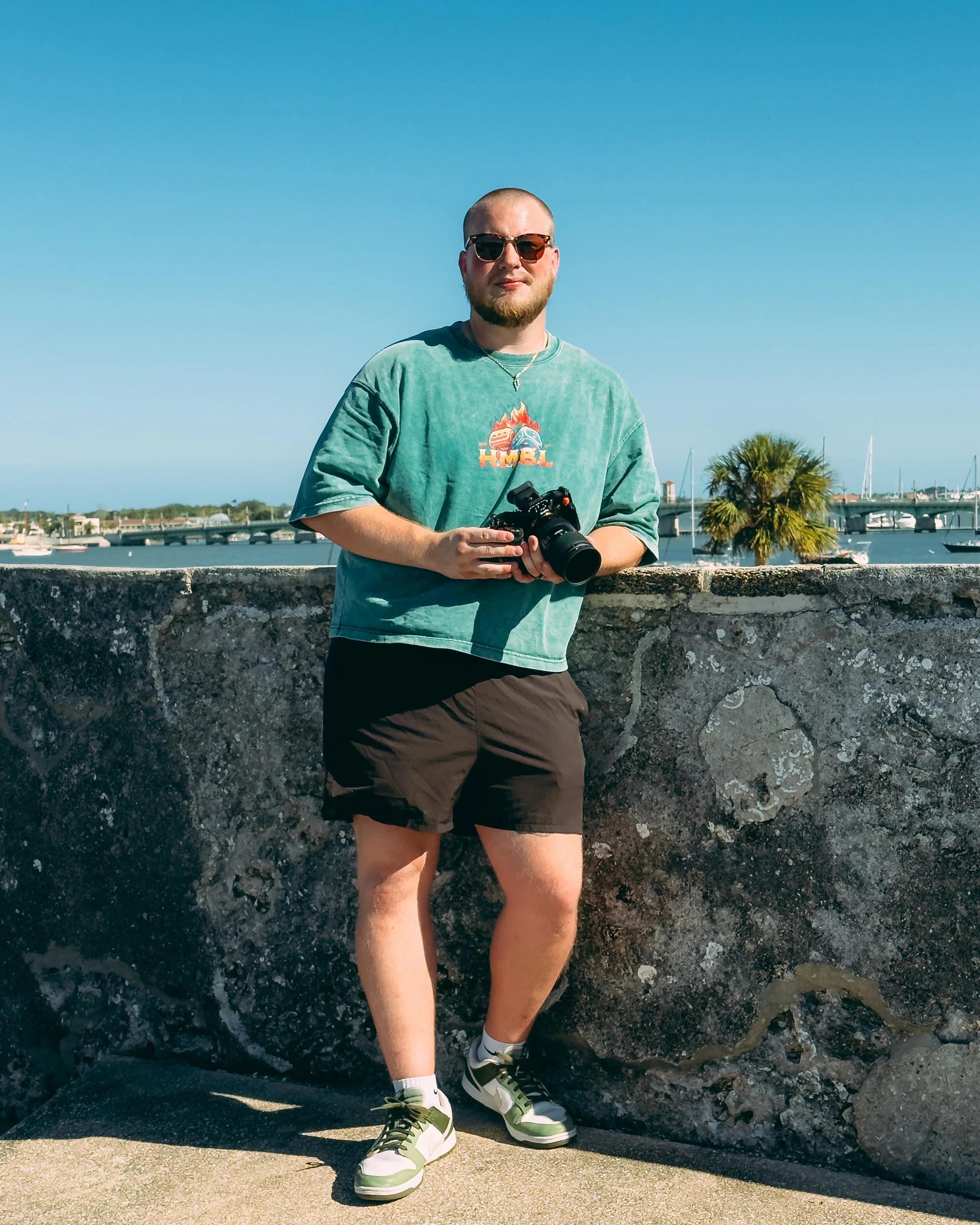 Brad holding a camera beside the water with boats and palm trees in the background while visiting St Augustine Florida