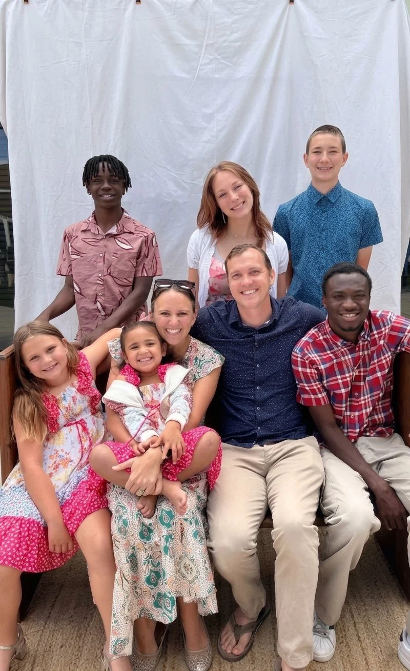 A group of eight people, including children and adults, gathered together, smiling, and posing for a photo in front of a white backdrop.