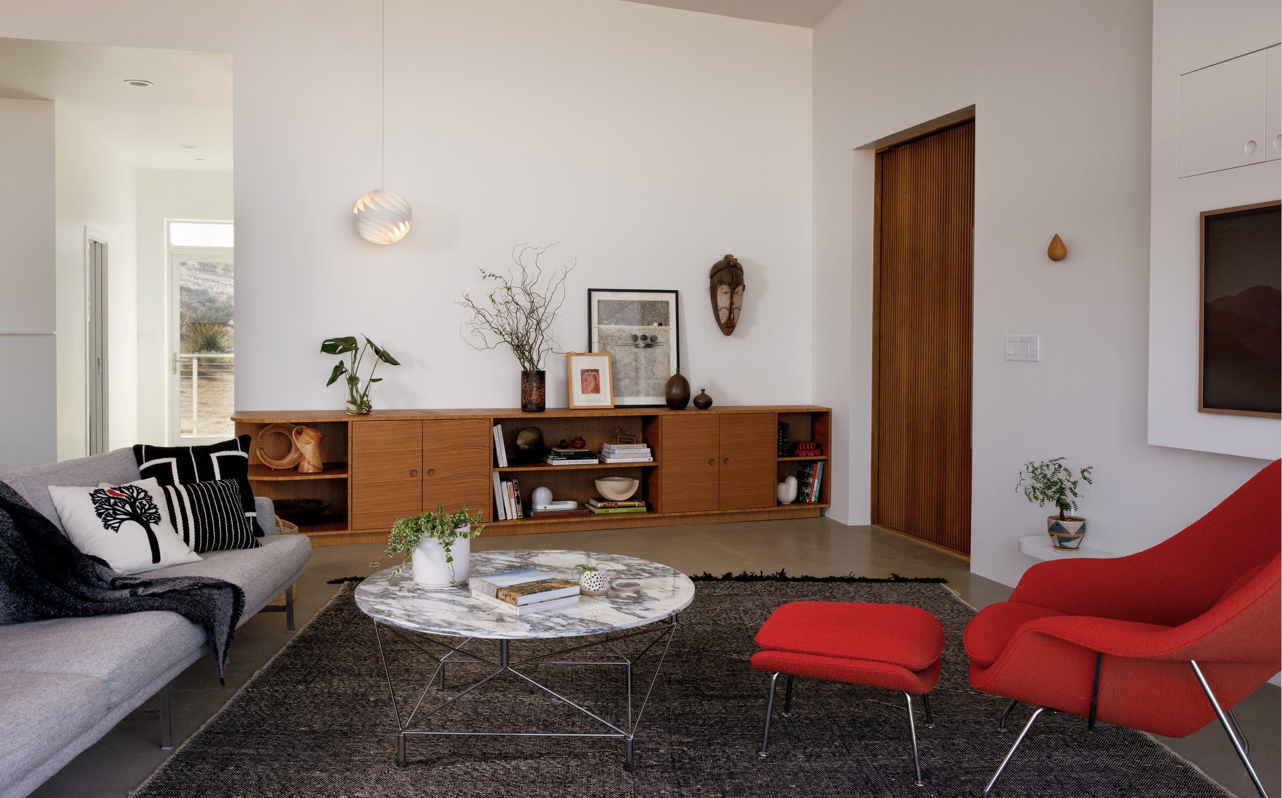 Living room at Panorama House featuring a Piero Lissoni sofa, red Womb Chair and ottoman, Andreas Hansen and Niels Eilersen Spider marble coffee table, and a 13-foot custom white oak credenza.