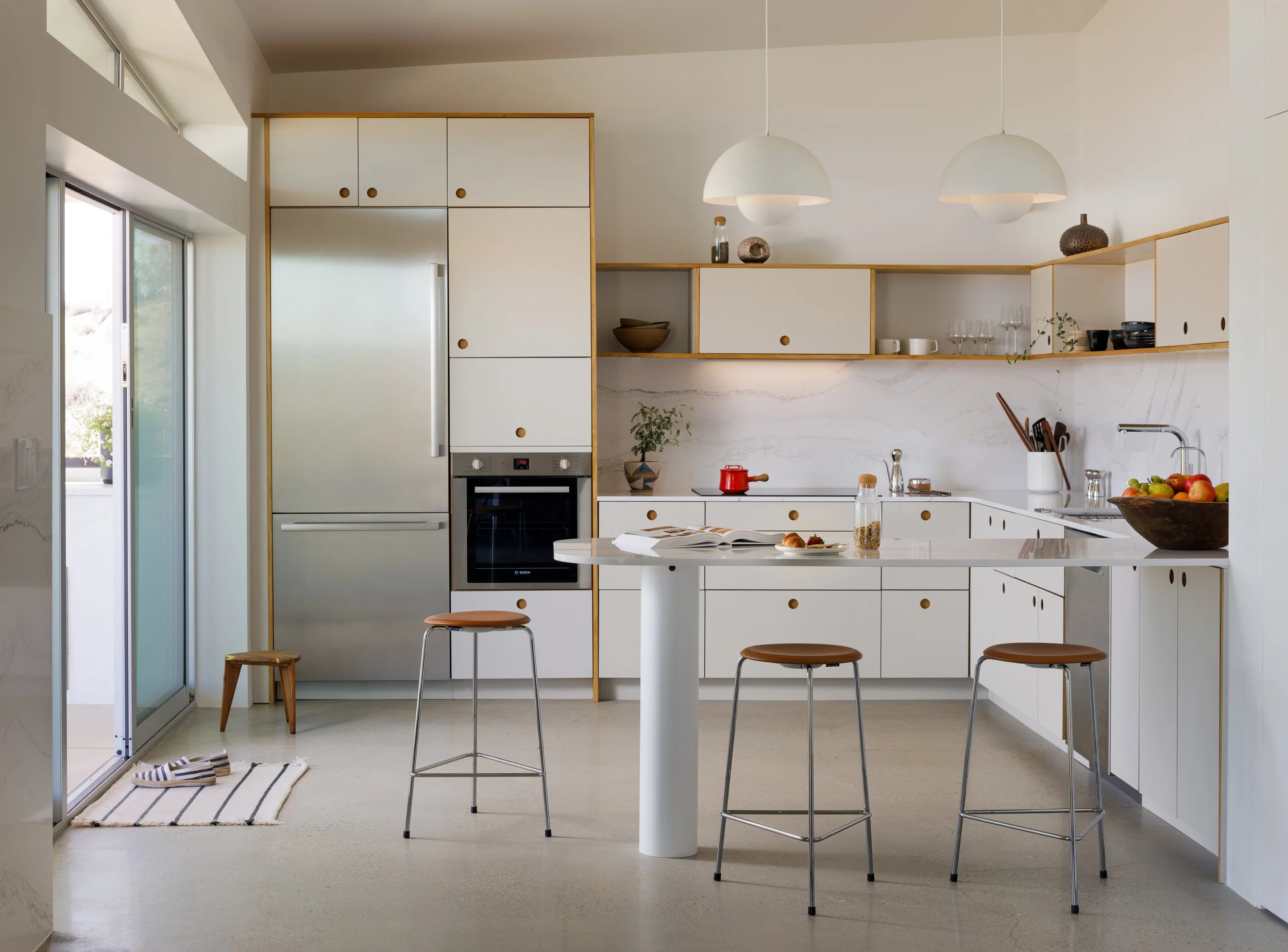Modern kitchen at Panorama House featuring white Reform cabinetry with natural wood trim, a Cambria quartz island, &Tradition Flowerpot pendant lights, Fritz Hansen Dot stools, and integrated Bosch appliances.