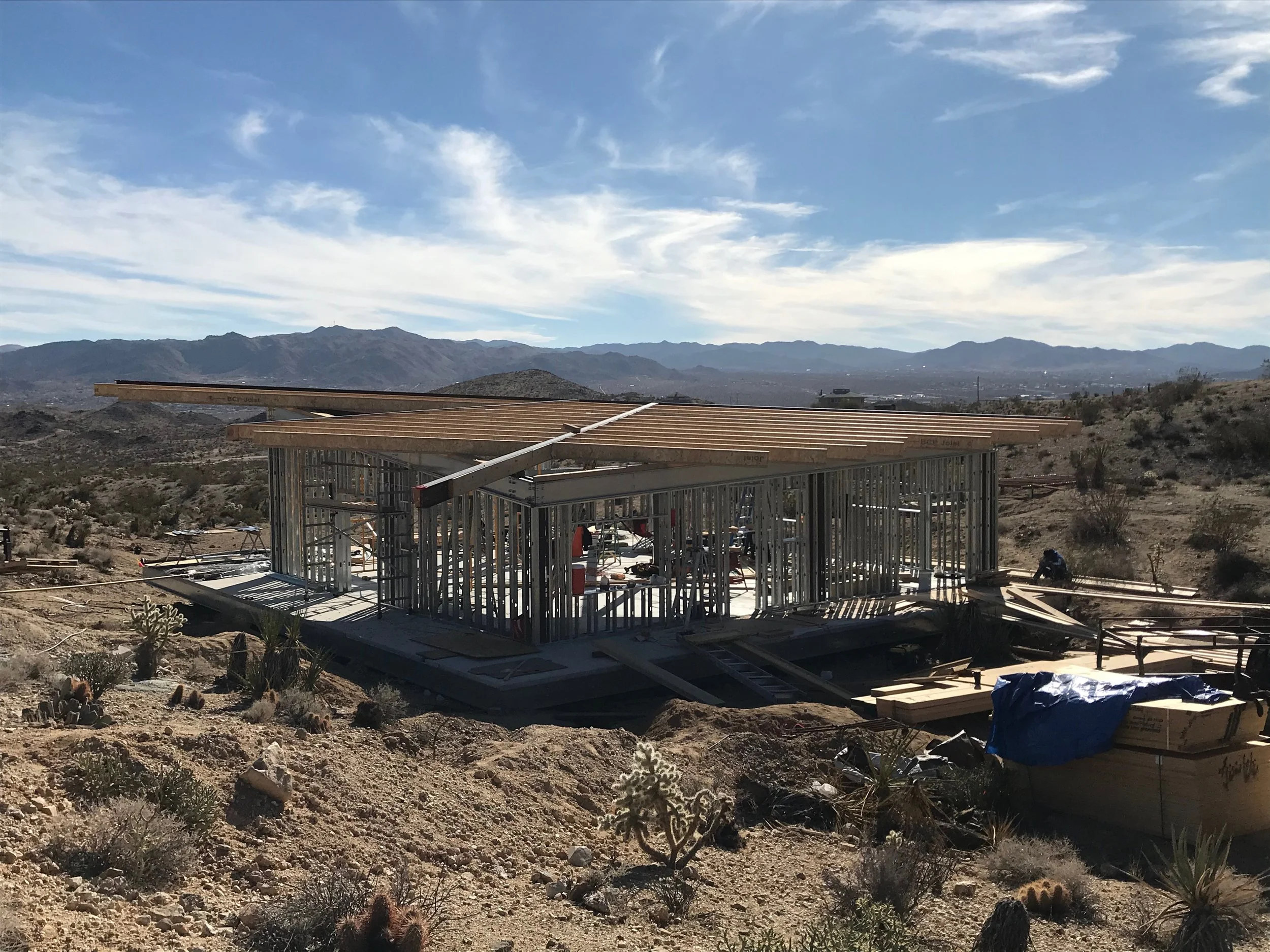 Panorama House under construction in Yucca Valley, showing TJI engineered wood roof joists spanning the steel-framed structure, surrounded by the Mojave Desert and distant mountains.
