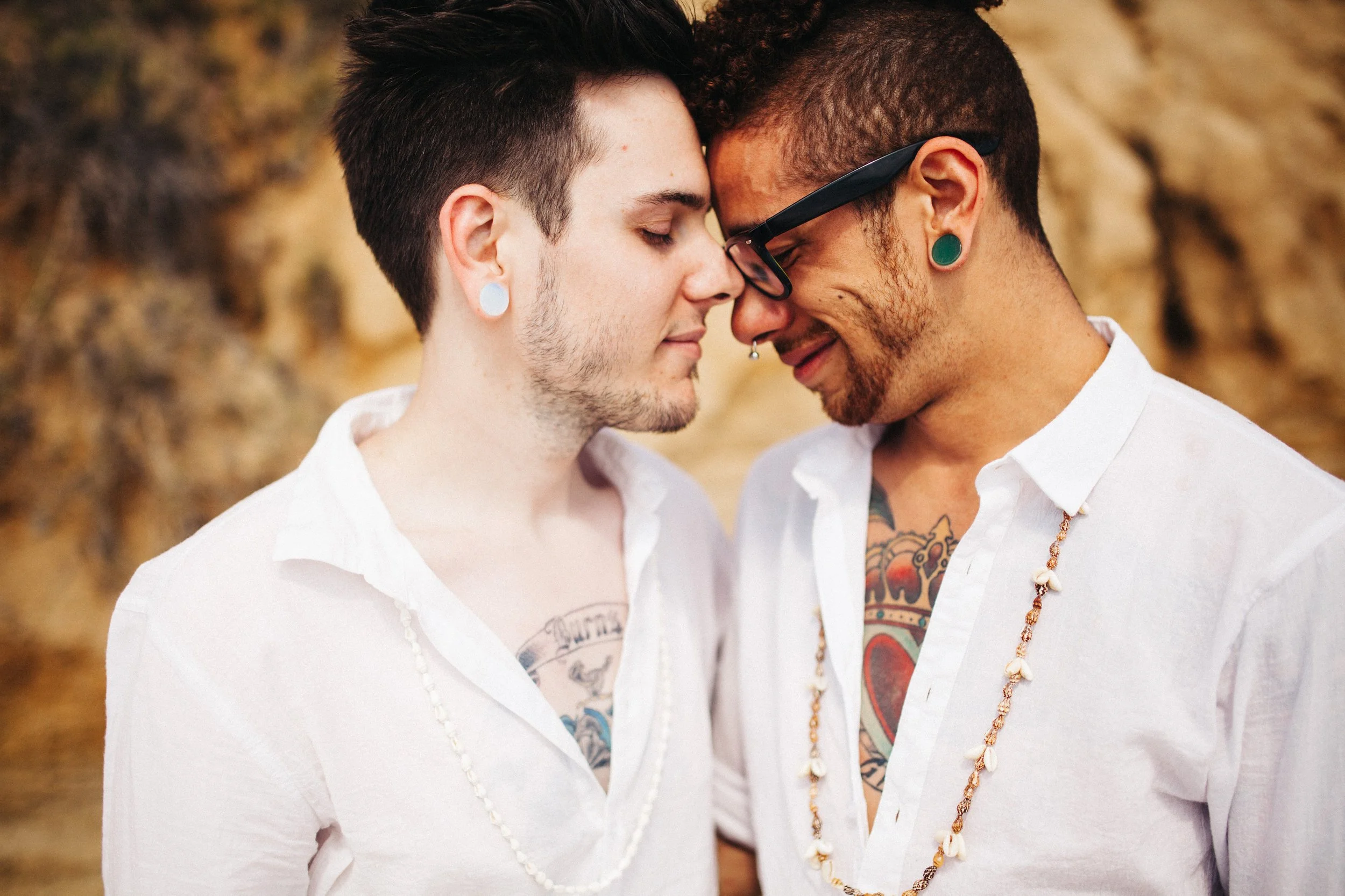 Two men with their foreheads and noses touching, eyes closed, sharing an intimate moment outdoors