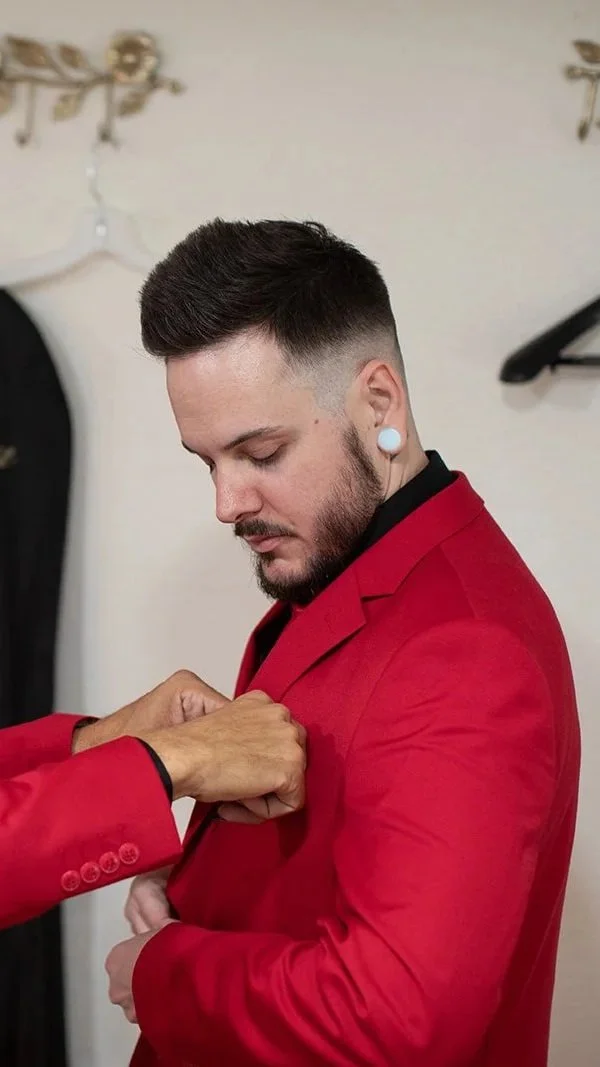 A man in a red suit having his jacket buttoned by another person.