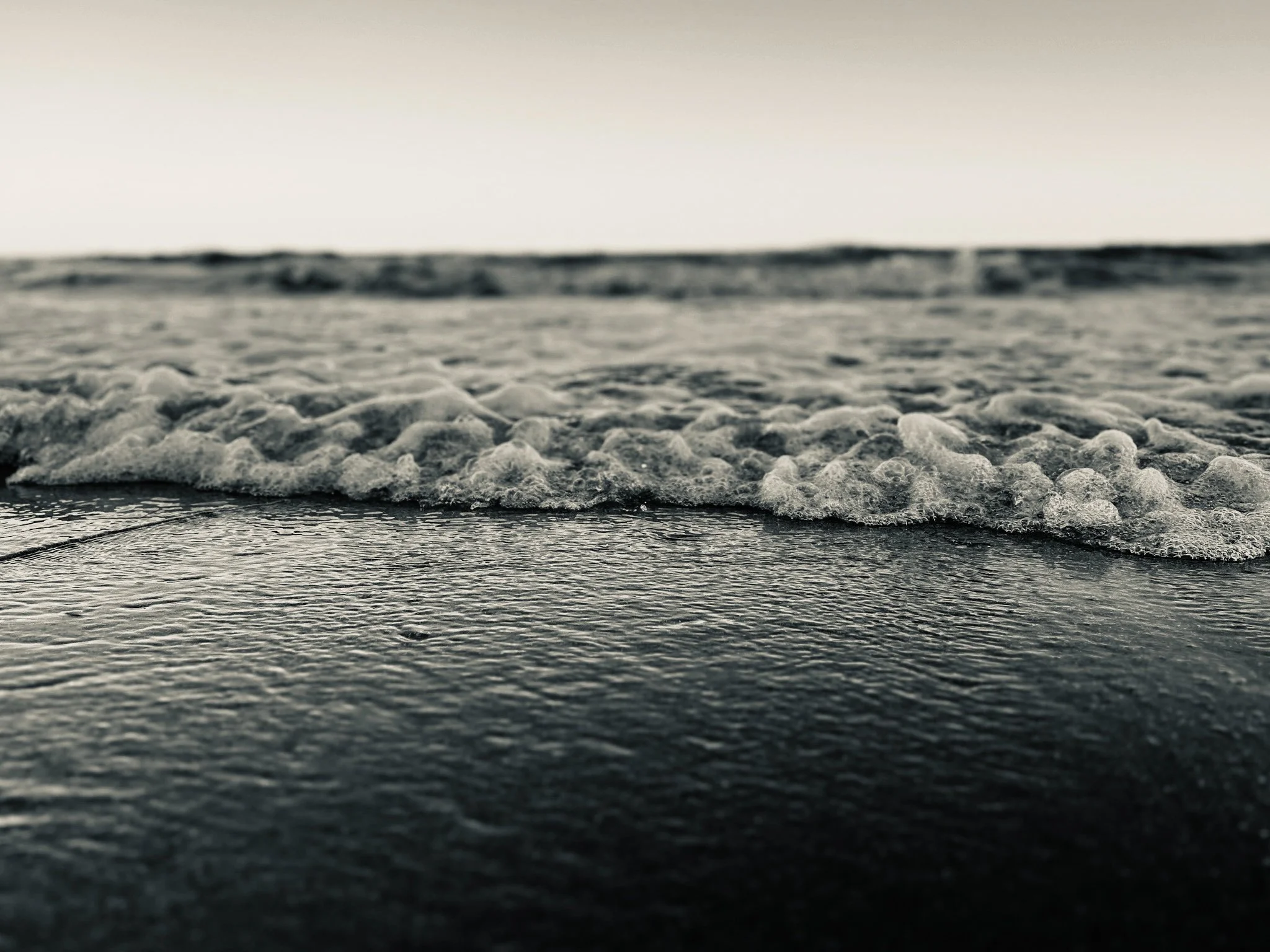 Close-up of ocean waves with foam on the surface, under a pale sky.