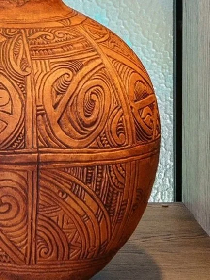 Detail of a Wi Taepa carved clay pot on a wooden shelf.