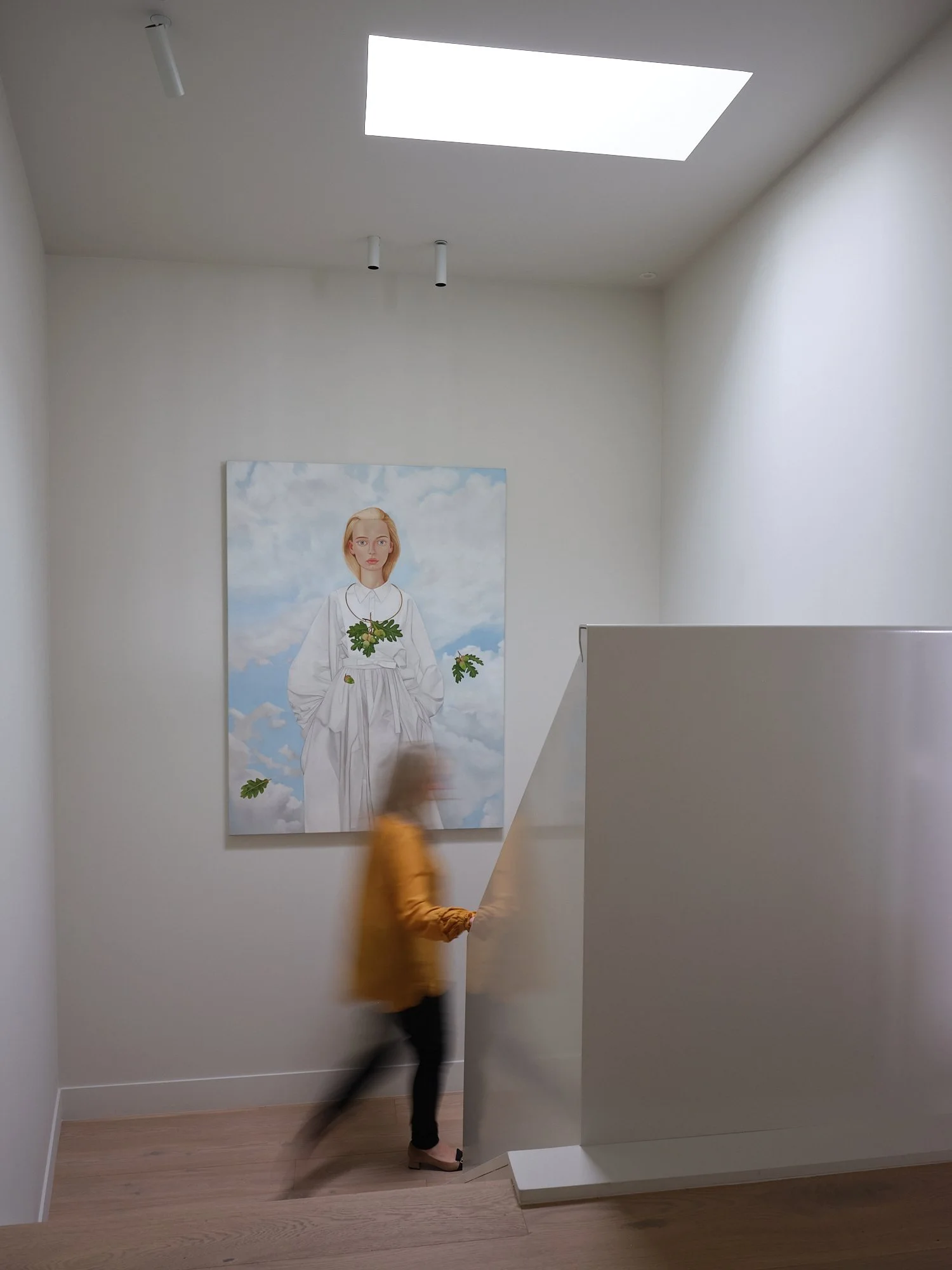 Large Michael Stichbury work on a wall in a stairwell with blurry figure walking past. 