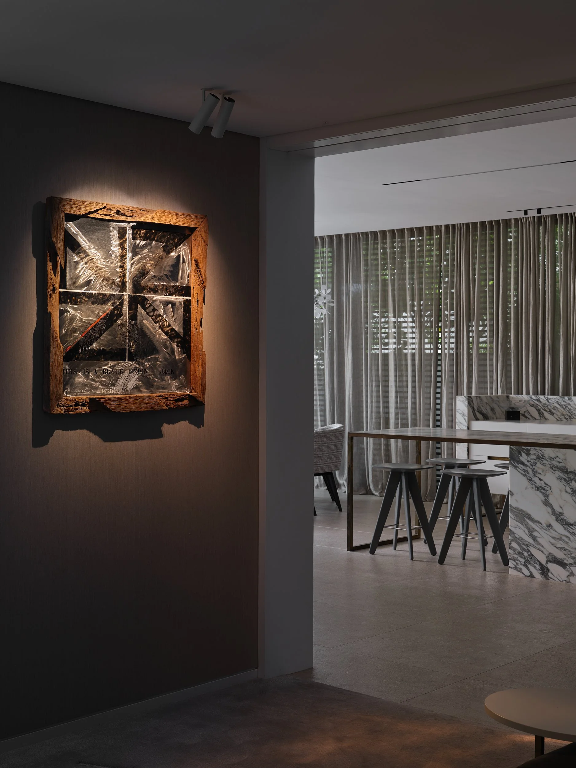 Spotlit artwork by Ralph Hotere on dark wall in a home.
