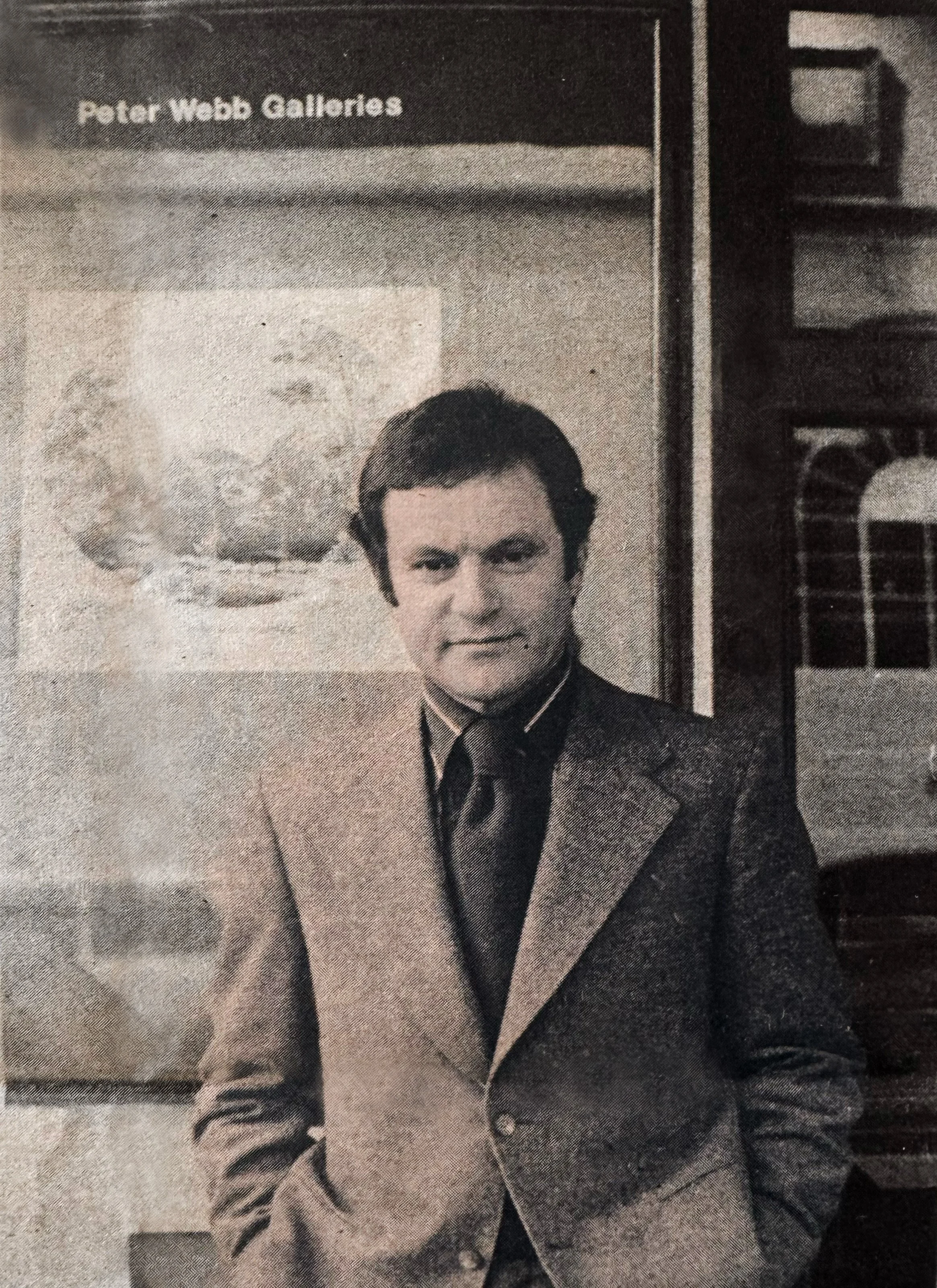 Black and white photograph of a young Peter Webb in a suit and tie, standing in front of Peter Webb Galleries