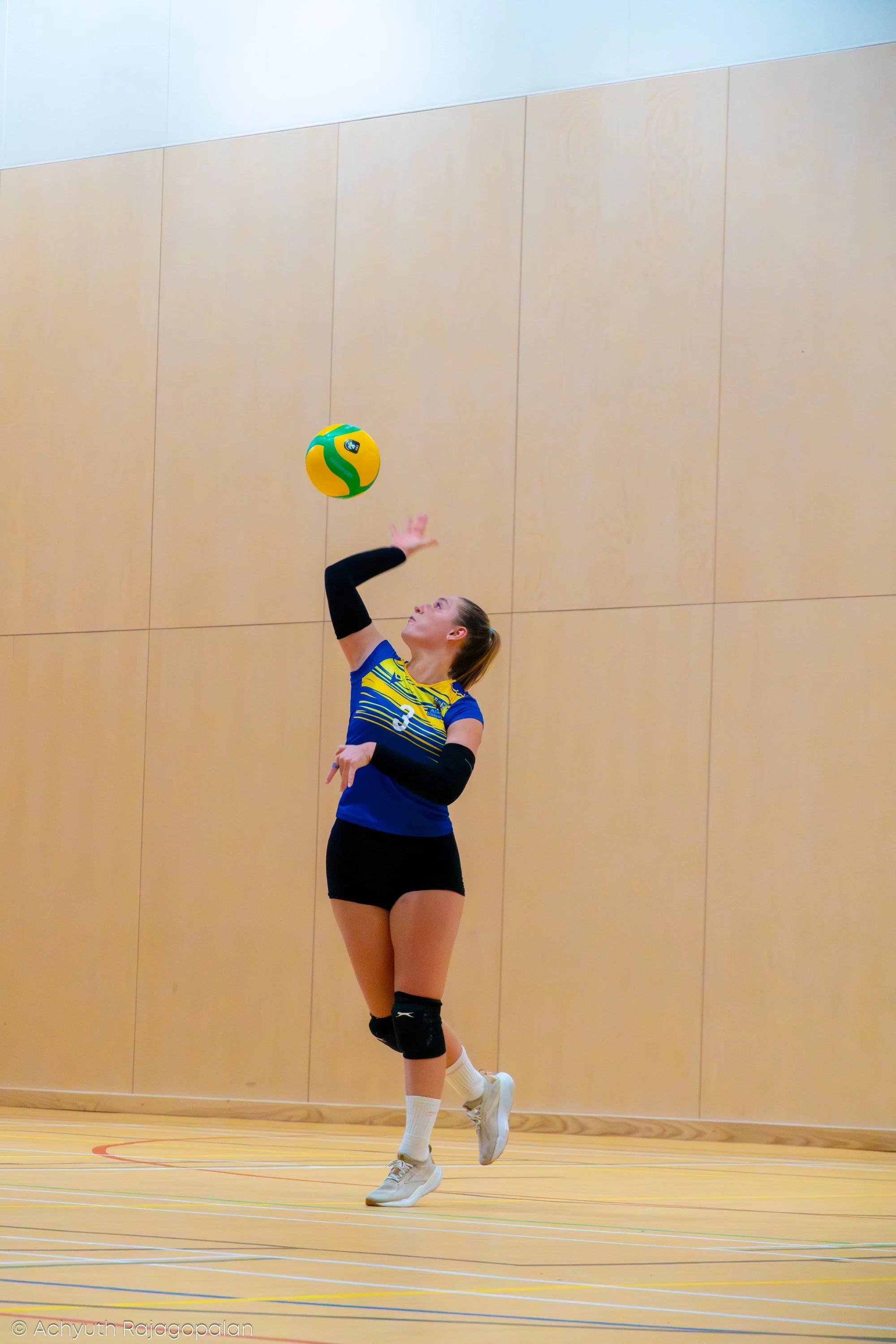 A female volleyball player in sports uniform spiking a yellow and green volleyball during an indoor match.