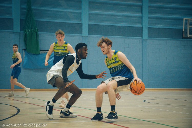 Two basketball players engaged in a game indoors, with two other players in the background.