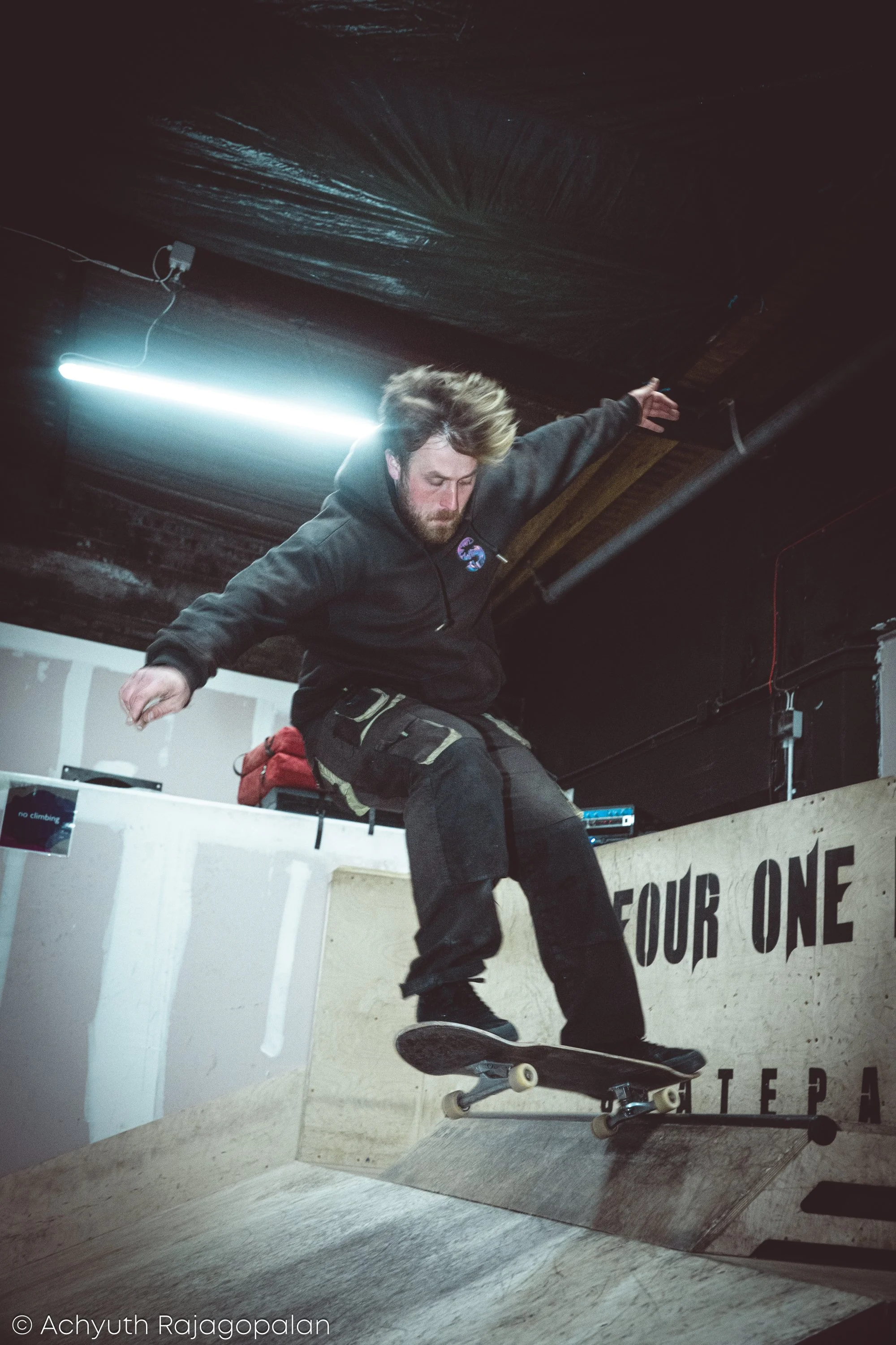 A man skateboarding in an indoor skatepark, performing a trick on a ramp.