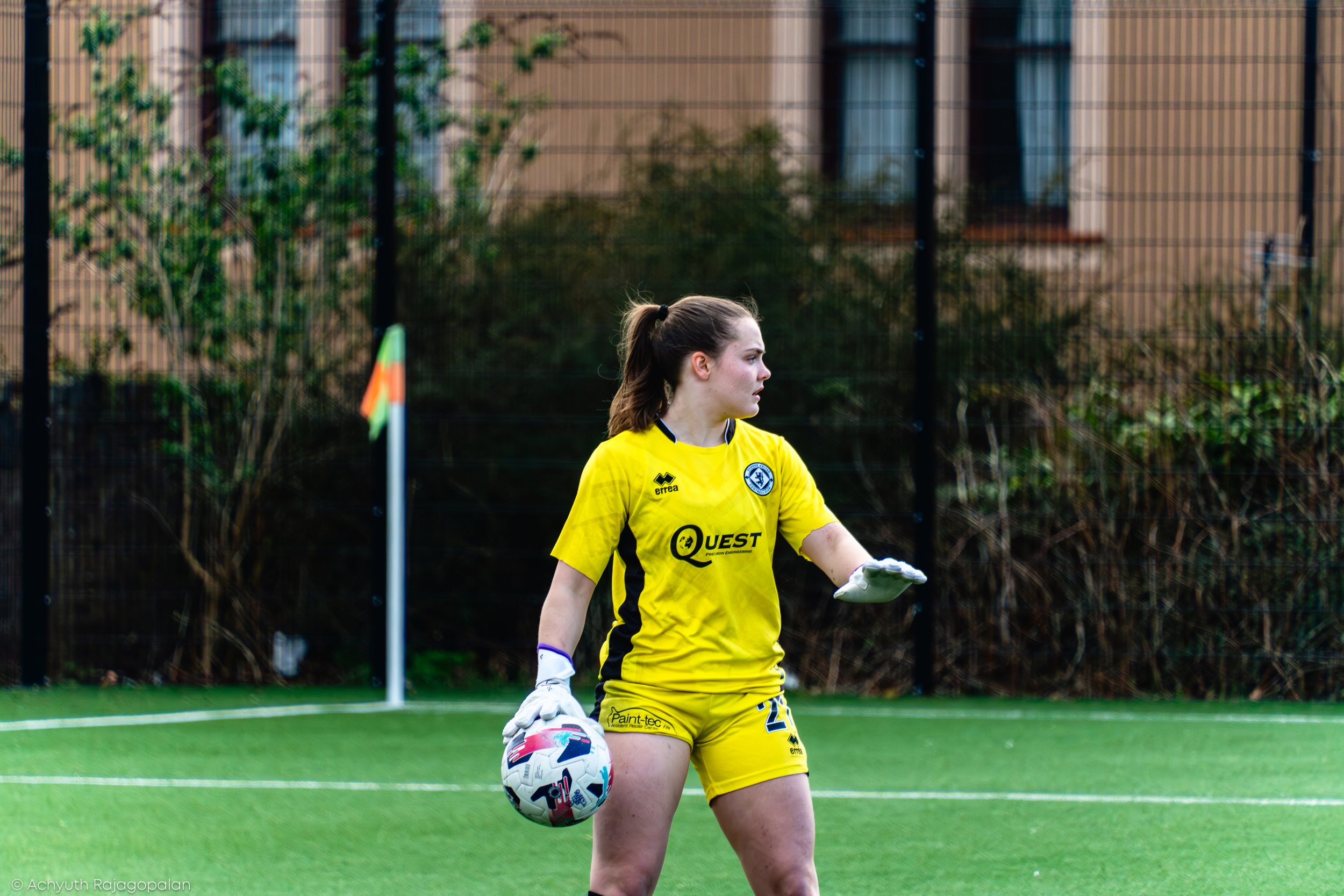 A female soccer player in a yellow uniform standing on a soccer field holding a soccer ball.
