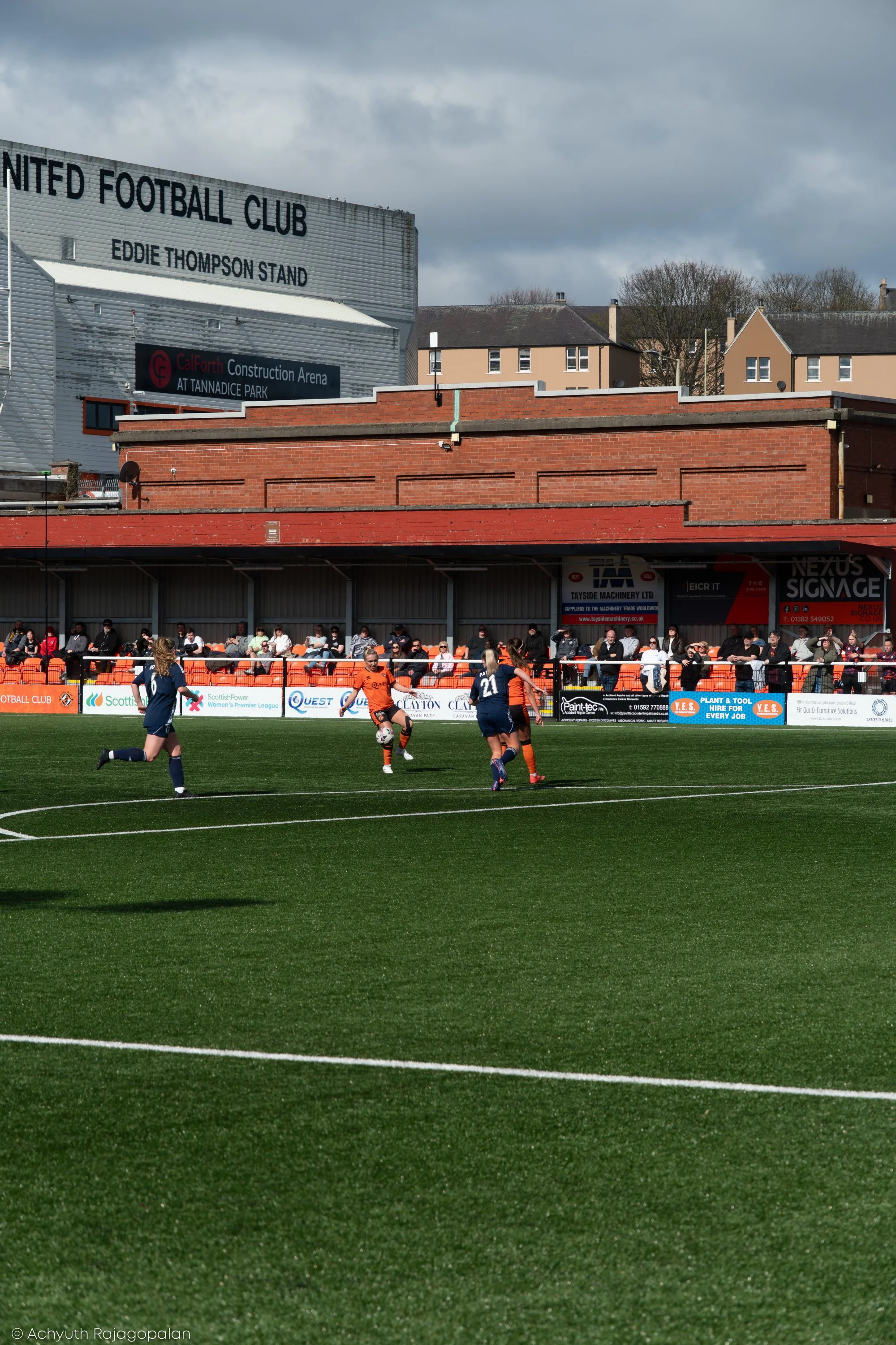 A soccer match taking place in a stadium with spectators and advertisements visible in the background. Players are on the field, actively participating in the game.