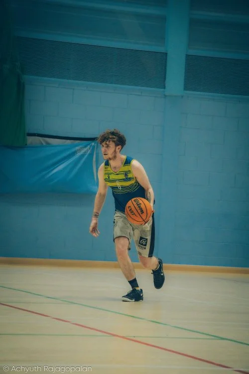 Young male basketball player dribbling a basketball on an indoor gym court.