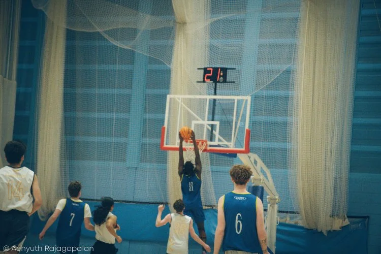 Children playing basketball in an indoor gym, with one child jumping to score a basket.