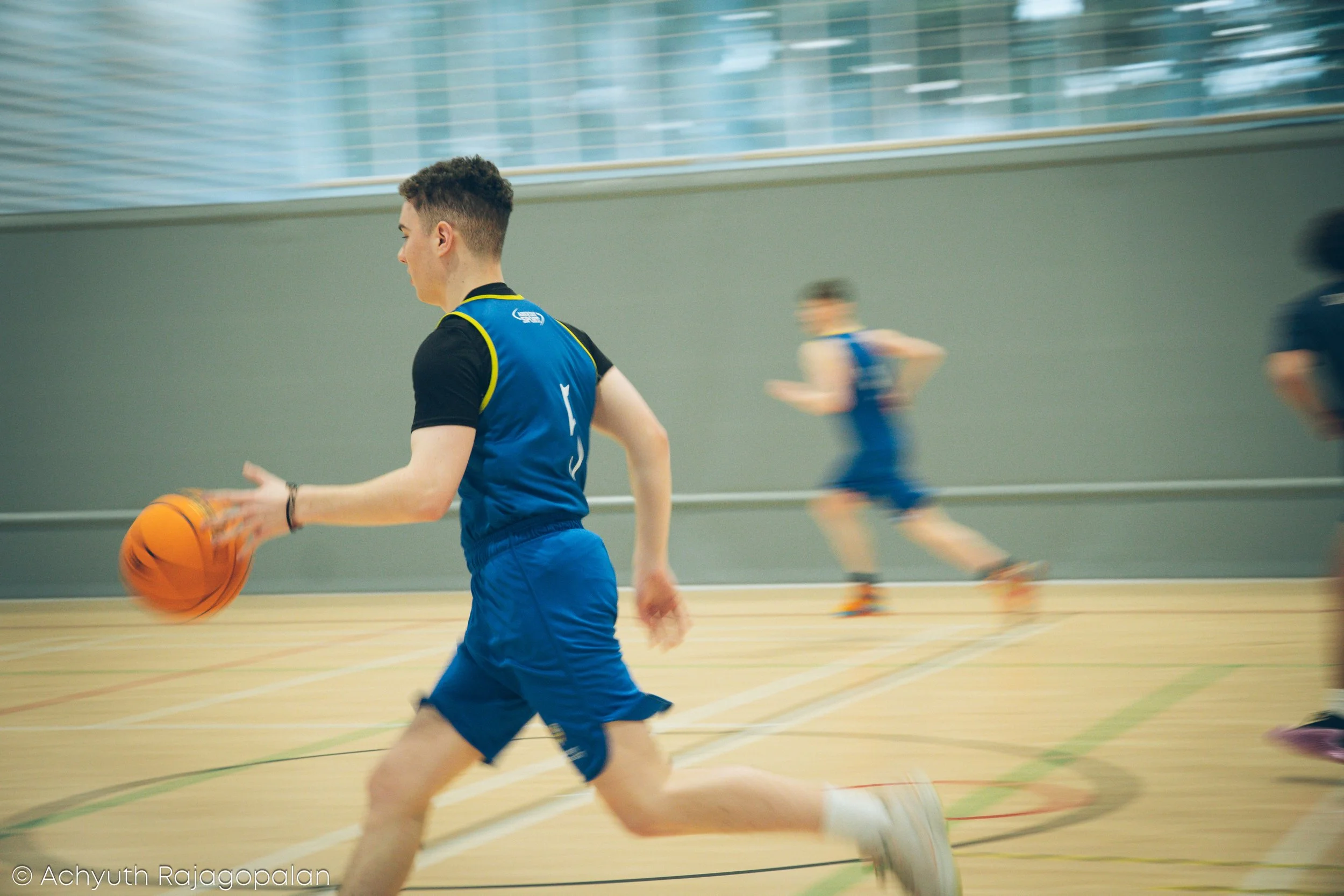 Young man playing basketball on an indoor court with other players in the background