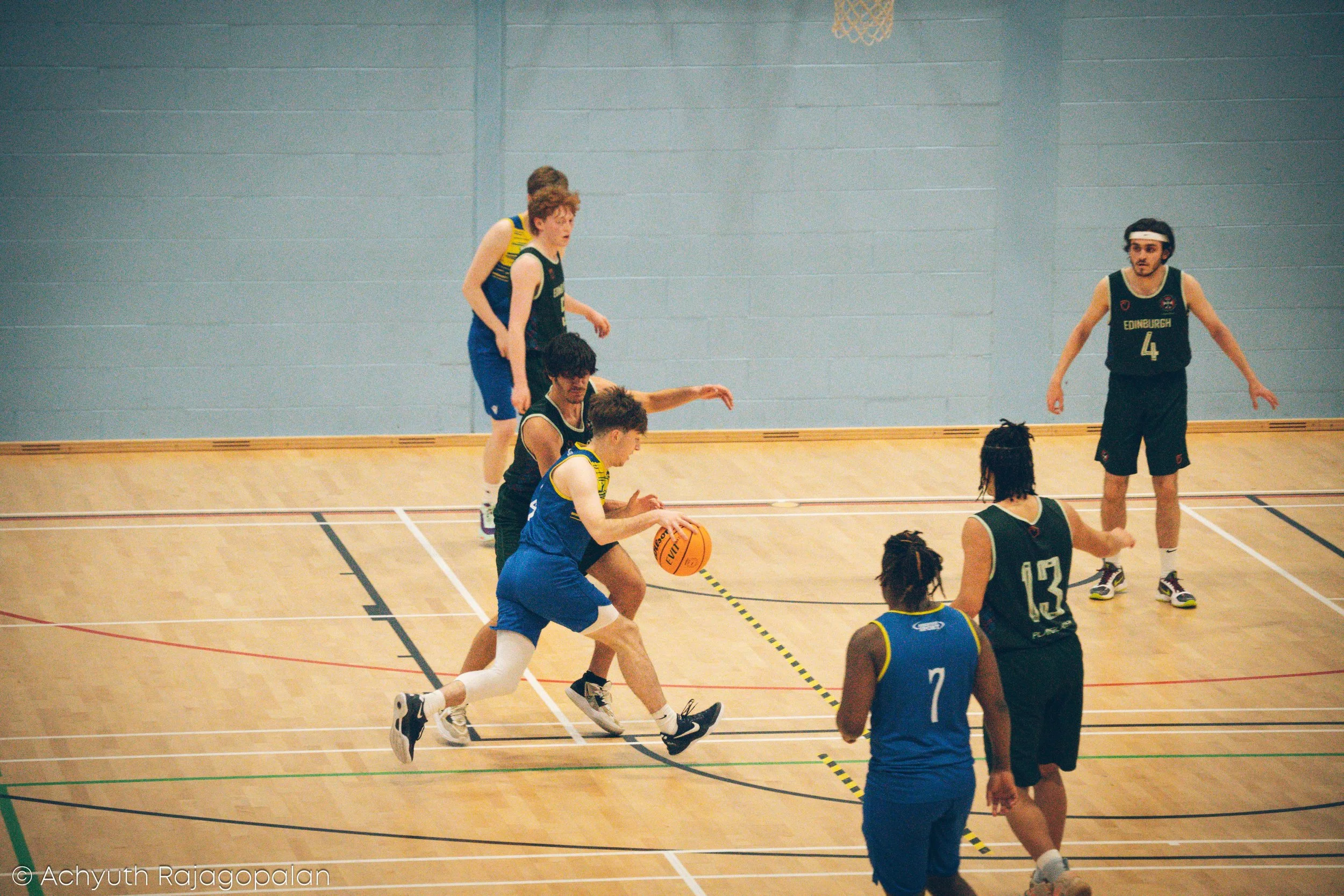 A youth basketball game with players in blue and black jerseys on an indoor court, actively competing for the ball, with some players reaching and jumping.