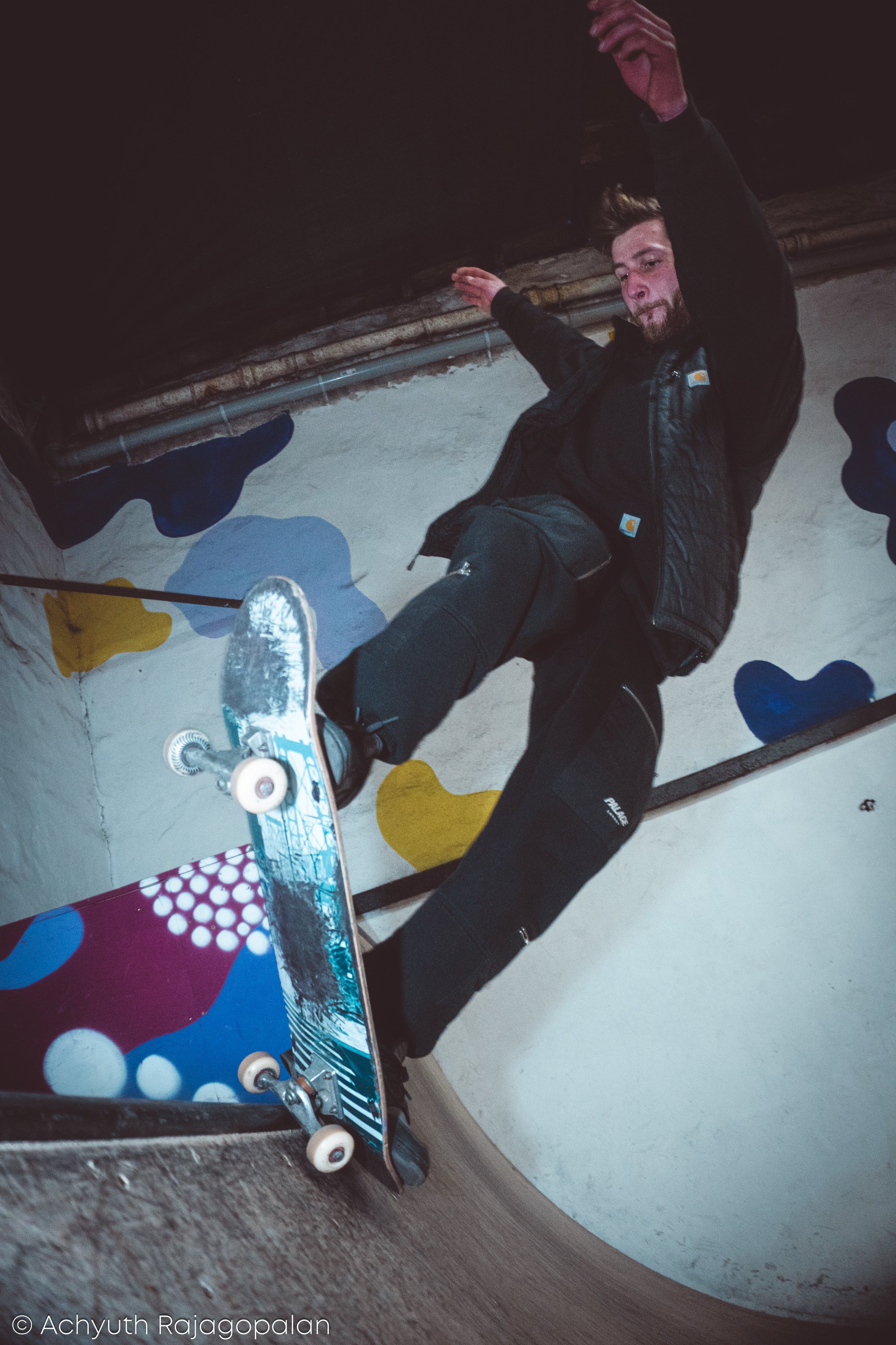 A young man skateboarding inside a building with colorful wall art.