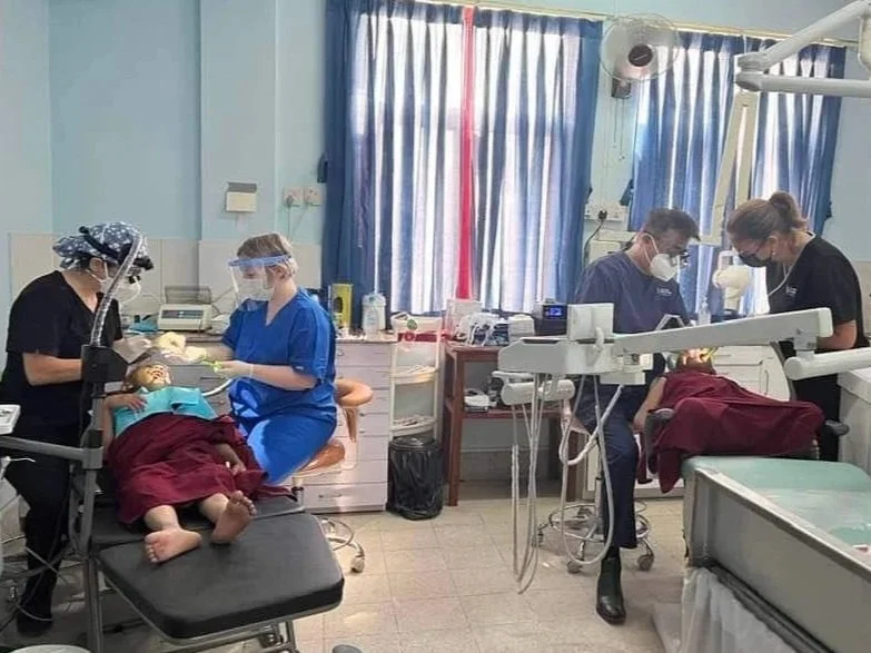 Gemma in scrubs with 3 other clinicians, working on two dental chairs, with two patients who are buddhist monks