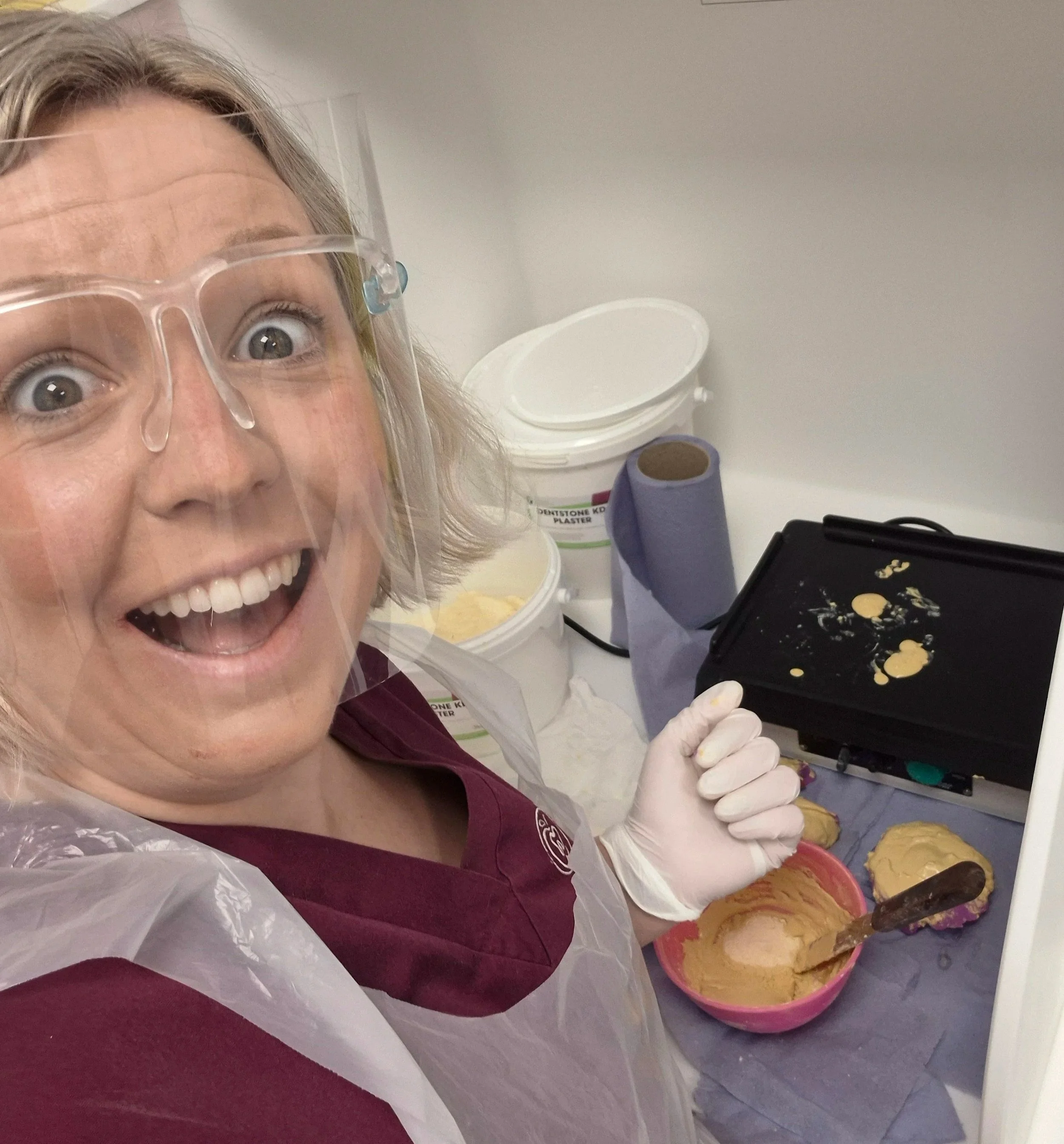 Gemma is in PPE including mask and apron. She is at a lab workstation pouring up plaster models.