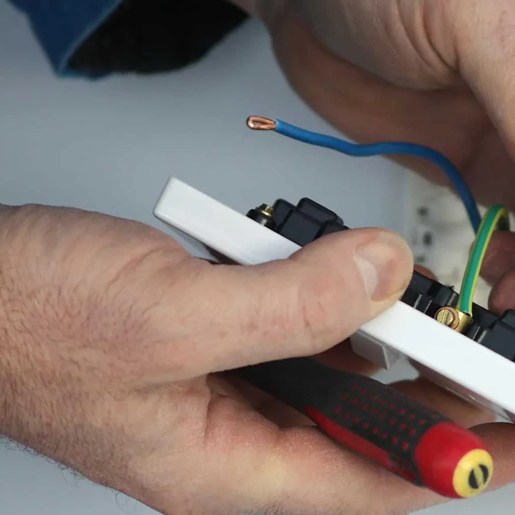 Close-up of a person holding electrical wires and a switch box, using a screwdriver.
