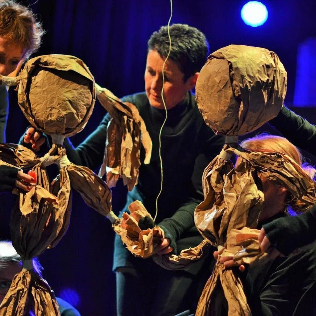 Mensen die een theatervoorstelling of poppenspel geven met grote poppen gemaakt van papier en karton.