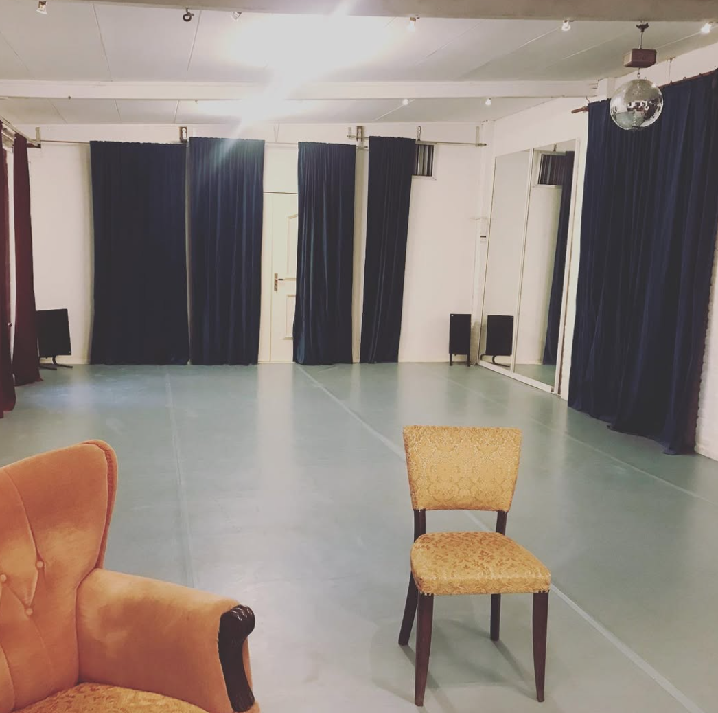Leeg danszaal met blauwe gordijnen, twee stoelen en een disco bal aan het plafond.