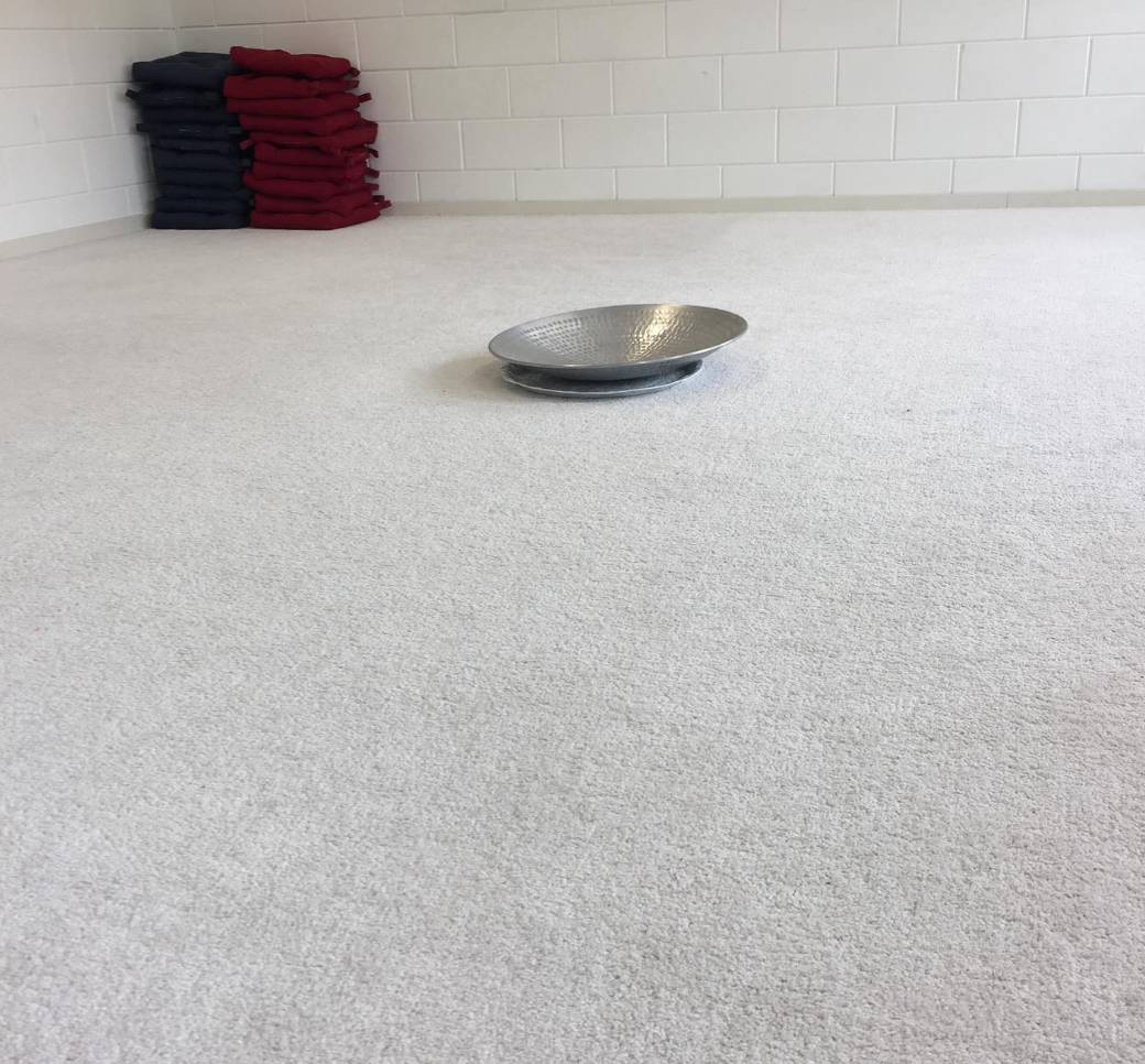 Stapel gekleurde kussens in zwart en rood op een witte muur, een metalen schaal op een witte vloer.