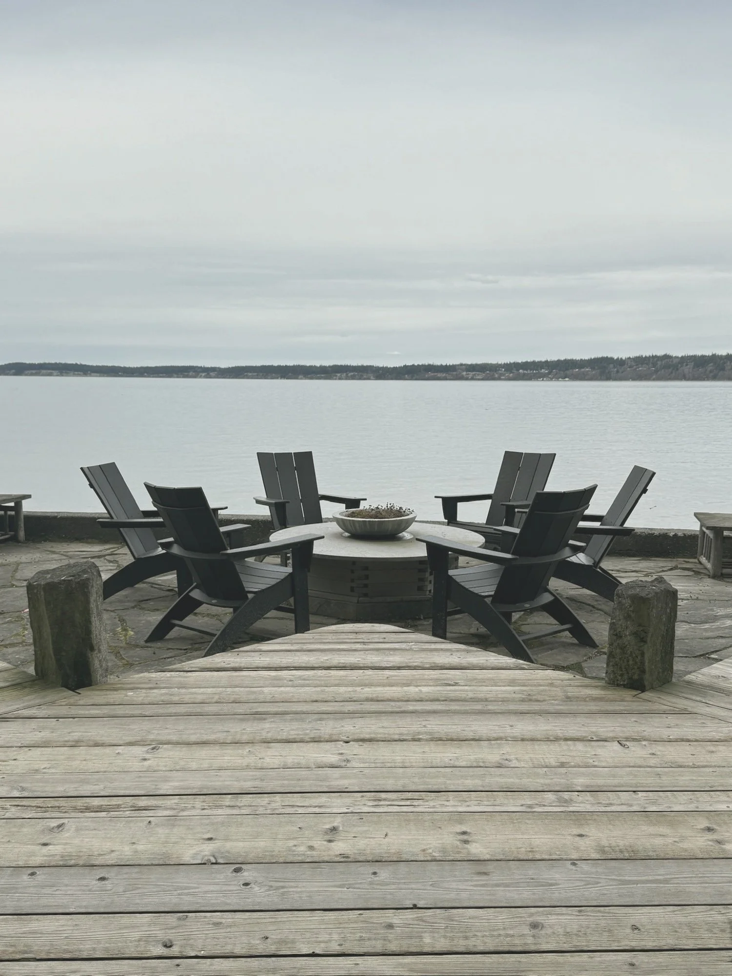 Circle of chairs around a fire pit facing calm water