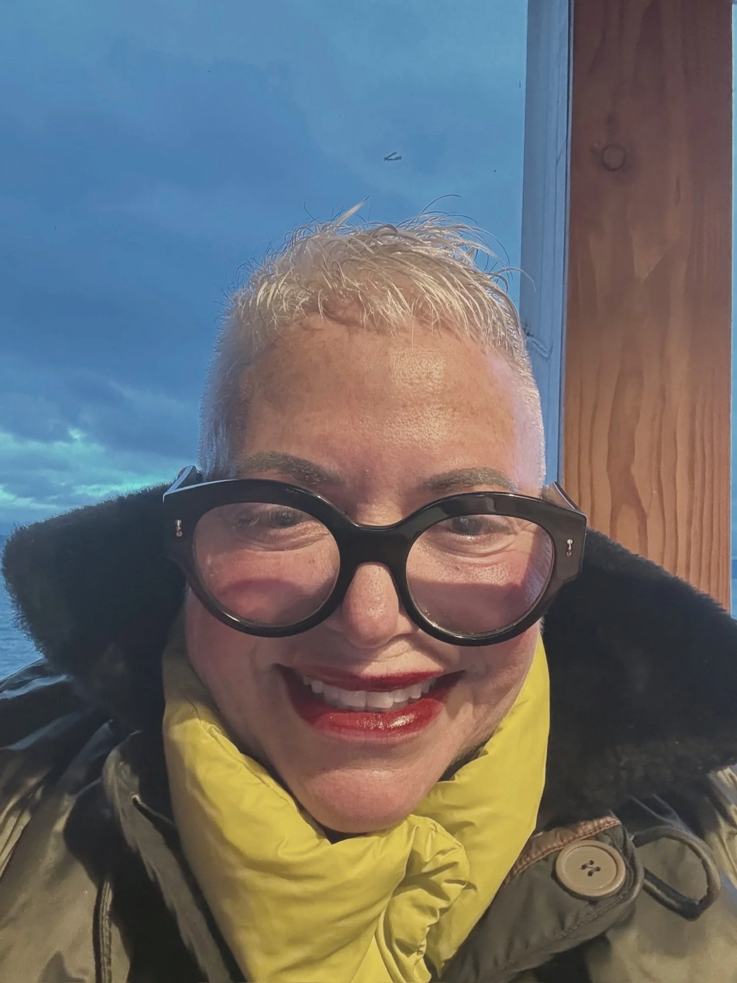 Eve Ruff smiling in round glasses and a yellow scarf on a ferry