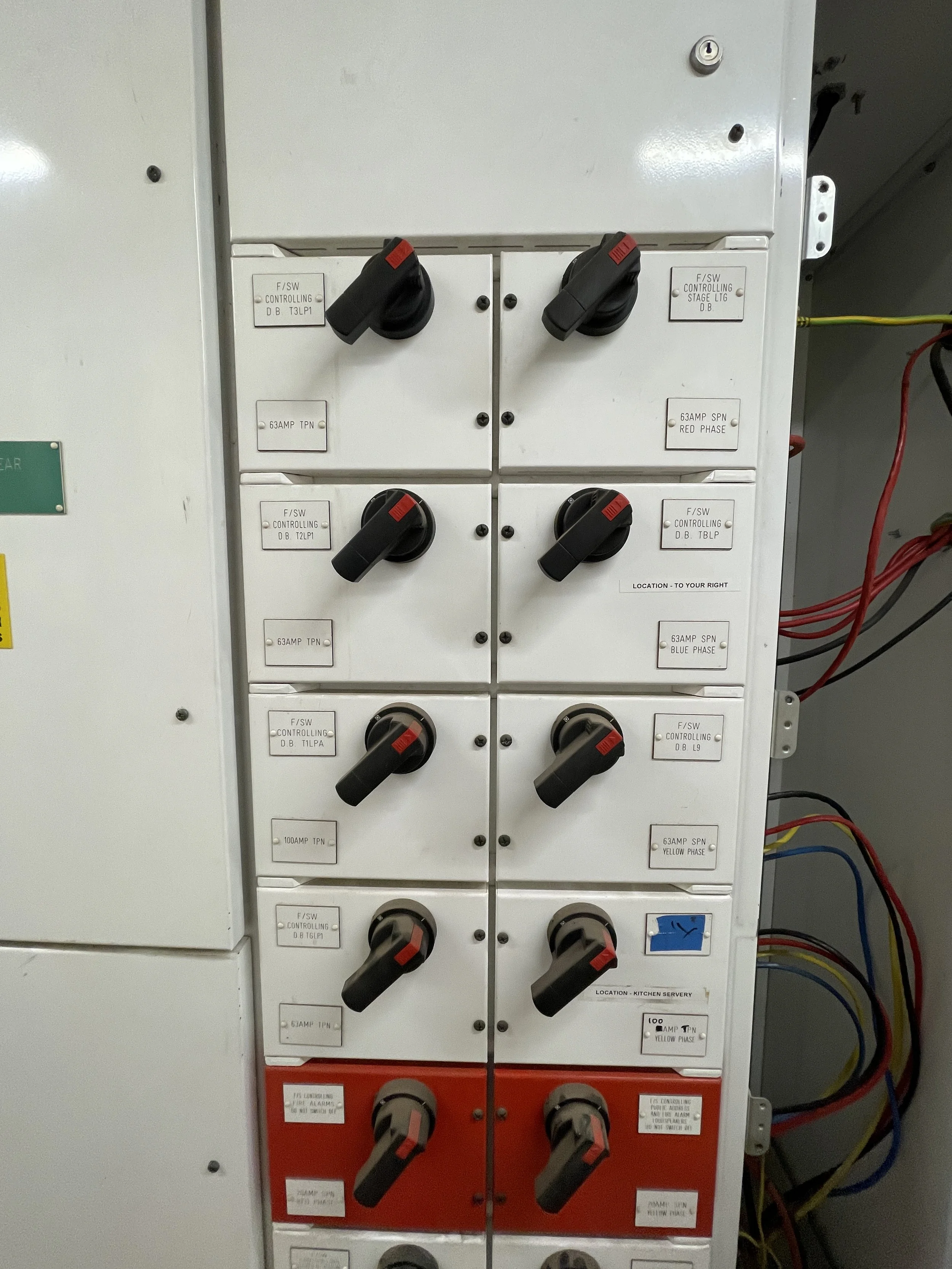 SOUTH LONDON COMMERCIAL ELECTRICIAN Close-up of an electrical control panel with multiple switches and labels indicating phases, amps, and locations, including kitchen and bathroom.