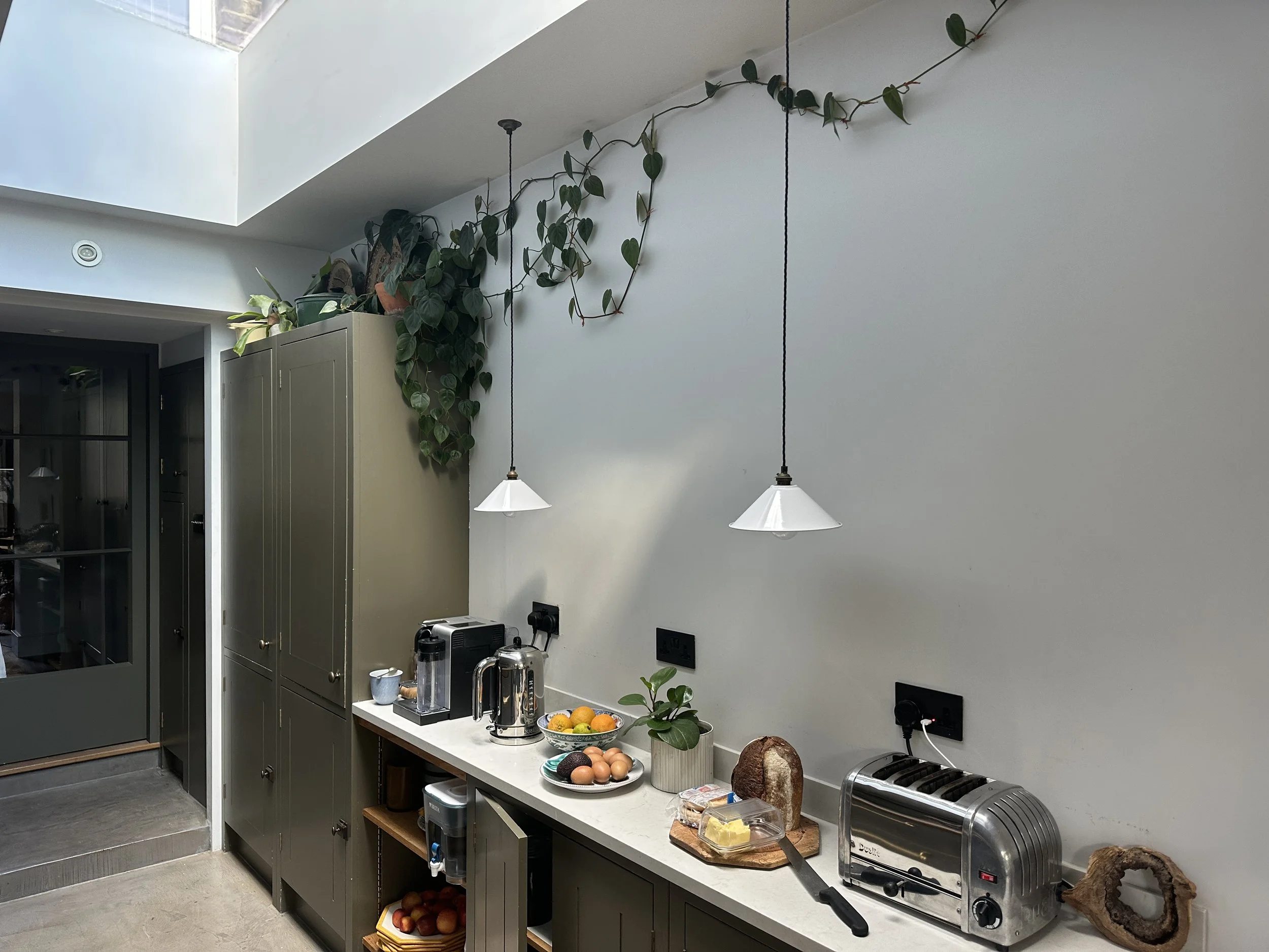 A kitchen countertop with a toaster, a loaf of bread, eggs, and a plant in a pot. There are two hanging pendant lights above, and kitchen cabinets and appliances in the background.