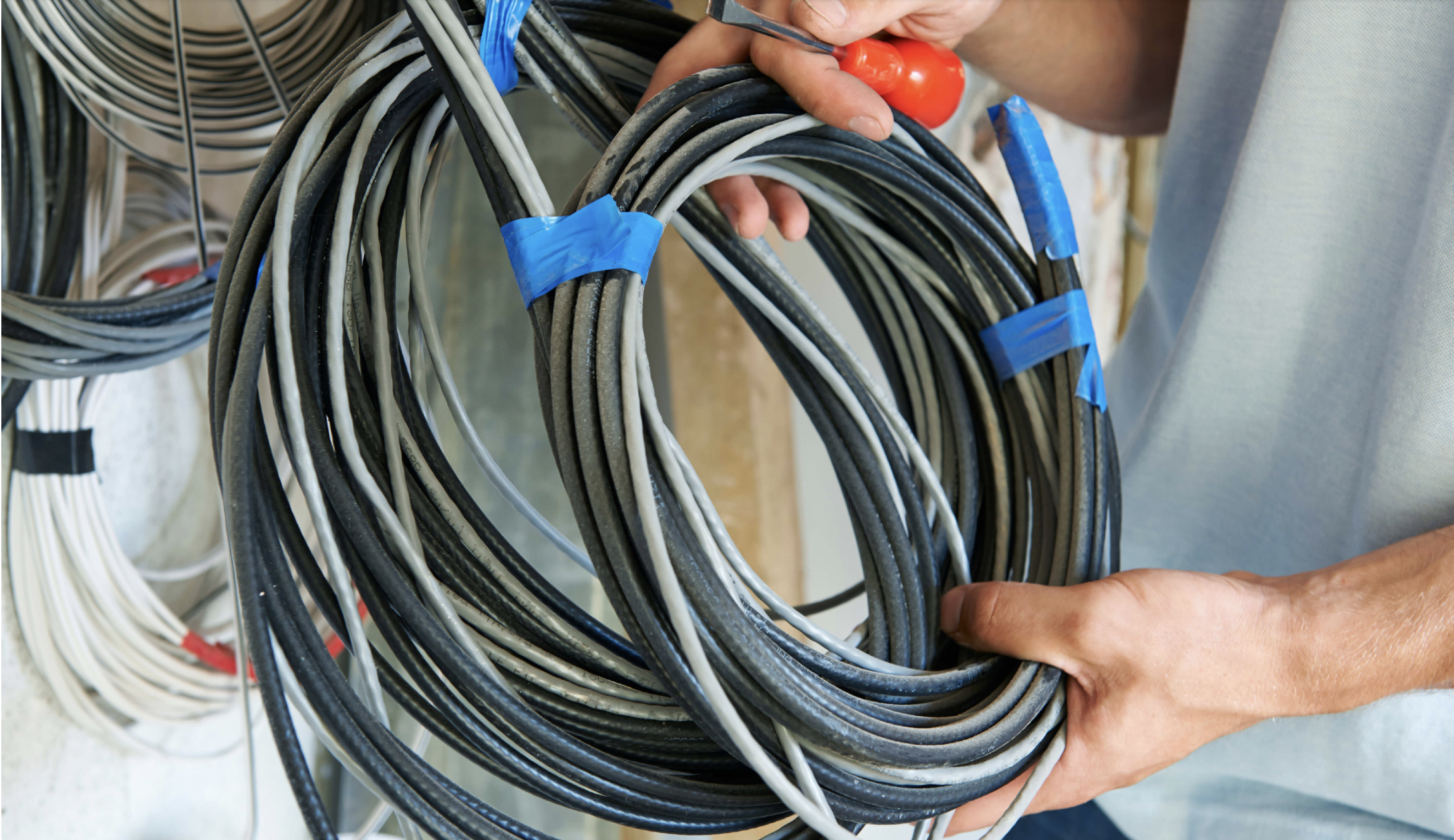 Person holding a coil of black, gray, and white electrical wires with blue tape.